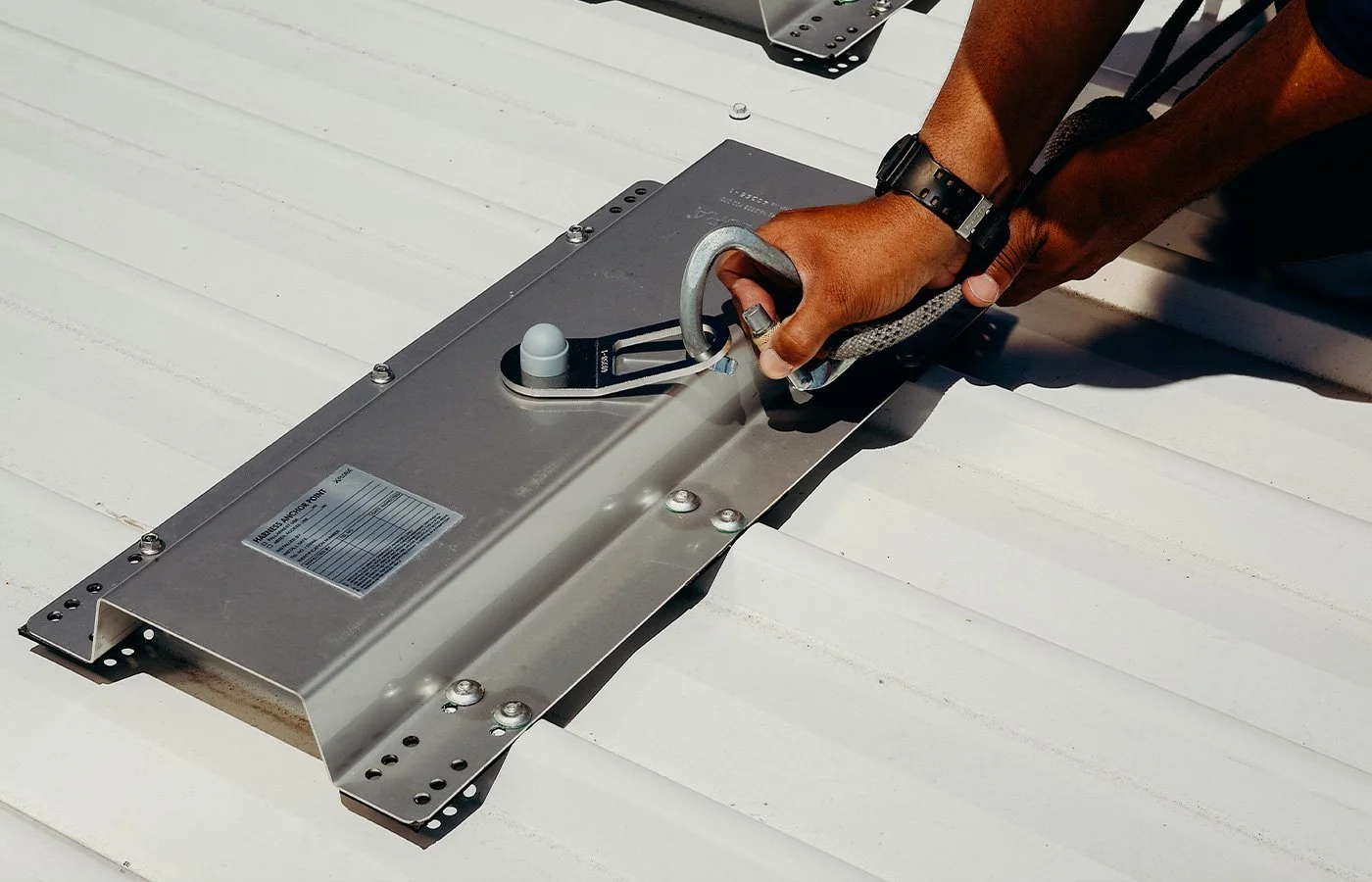 Person installing a roof anchor safety component on a white exterior surface using a hand tool.