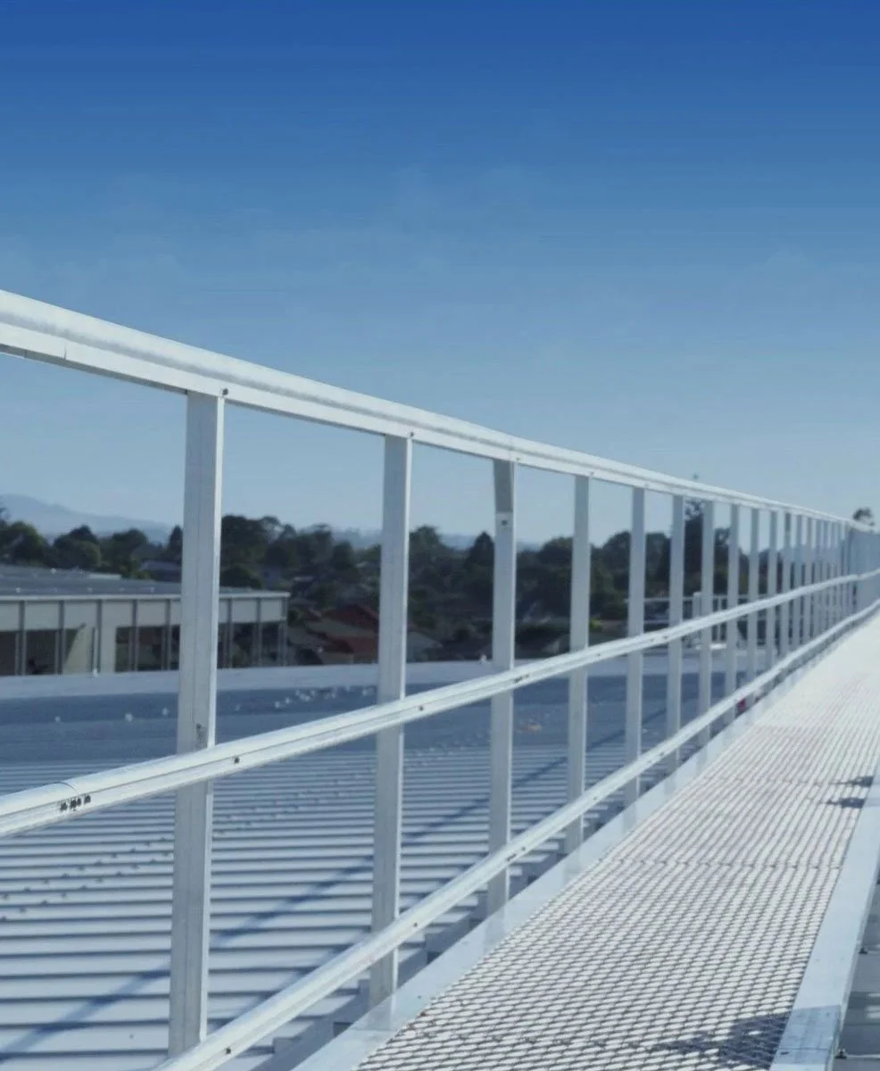 View from a rooftop with white metal railing and floor, overlooking a cityscape with trees and buildings under a clear blue sky.