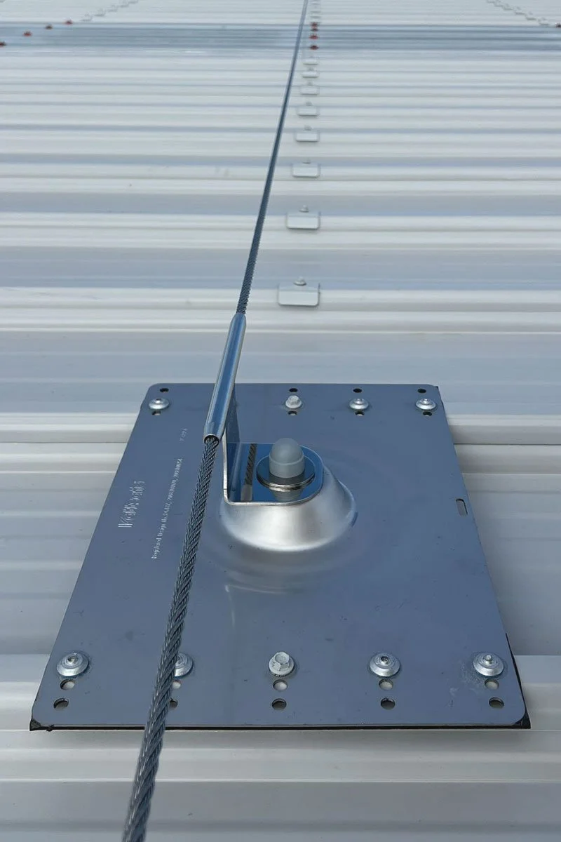 Close-up of a rooftop mount with a steel cable attached, a horizontal lifeline on a metal roof.