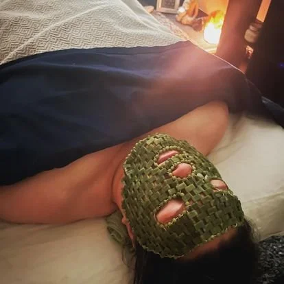 Person lying on massage table wearing a cooling Jade Stone Mask, covered partially by a blanket.