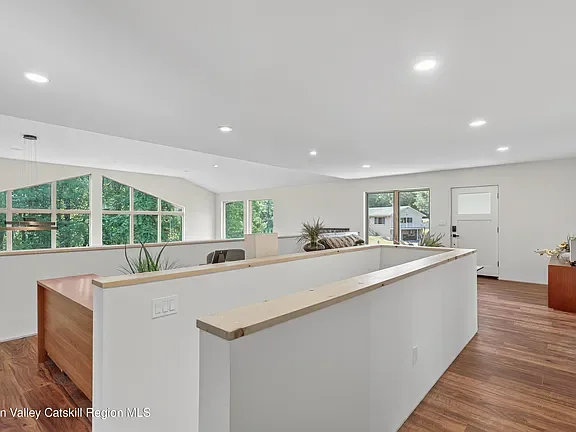 Open second-floor living space with wood floors, a half-wall railing and large forest-view windows