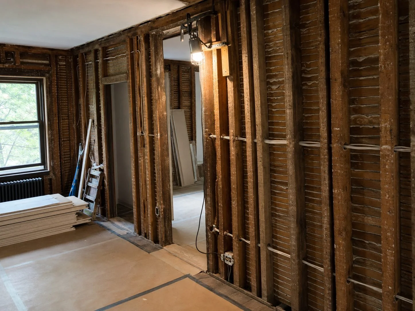Older Hudson Valley home mid-renovation with exposed balloon framing, original plaster lath, neatly routed electrical wiring, protected floors, and organized materials.
