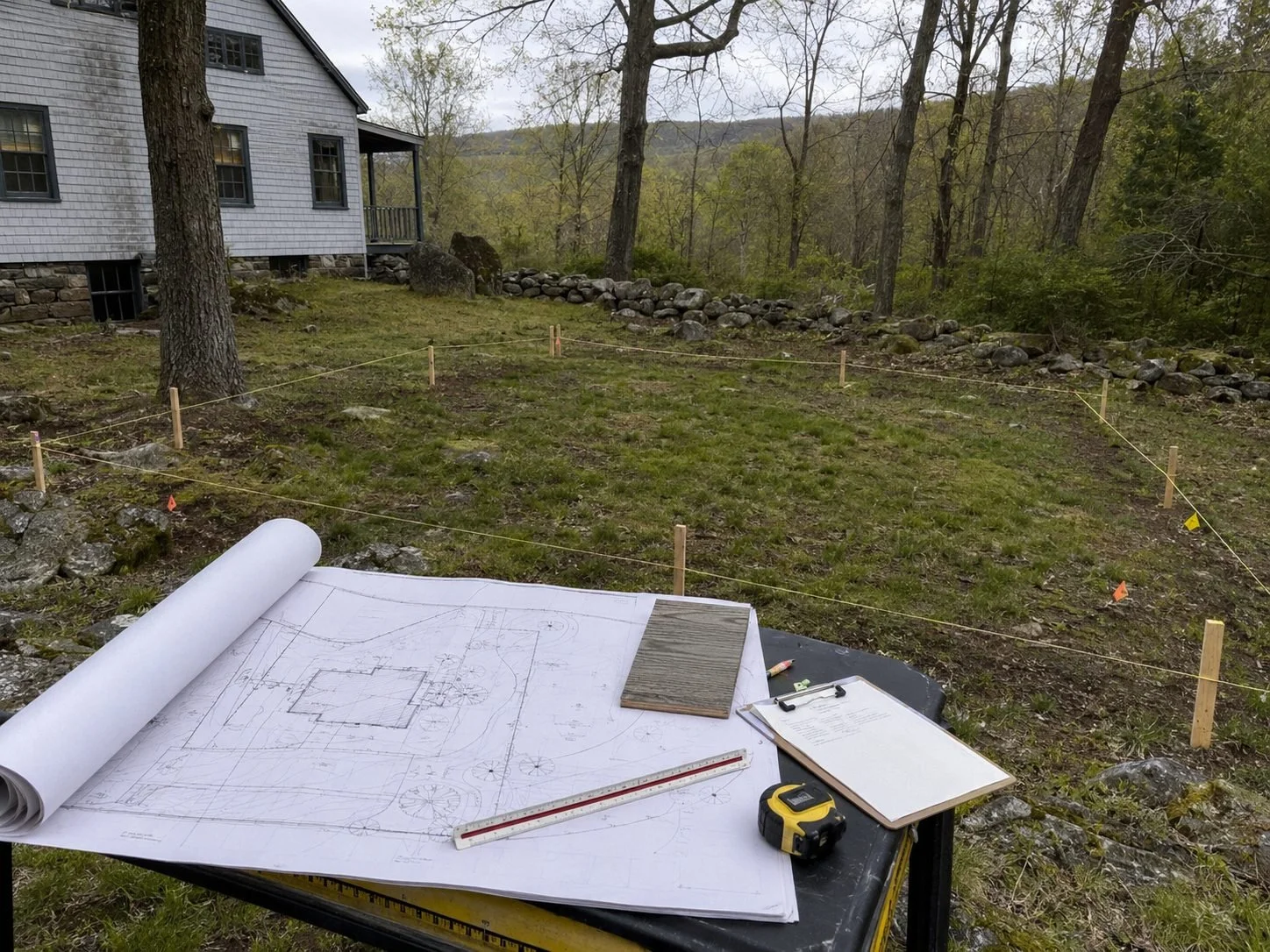 Architectural plans overlooking a staked ADU footprint on a wooded Hudson Valley property.