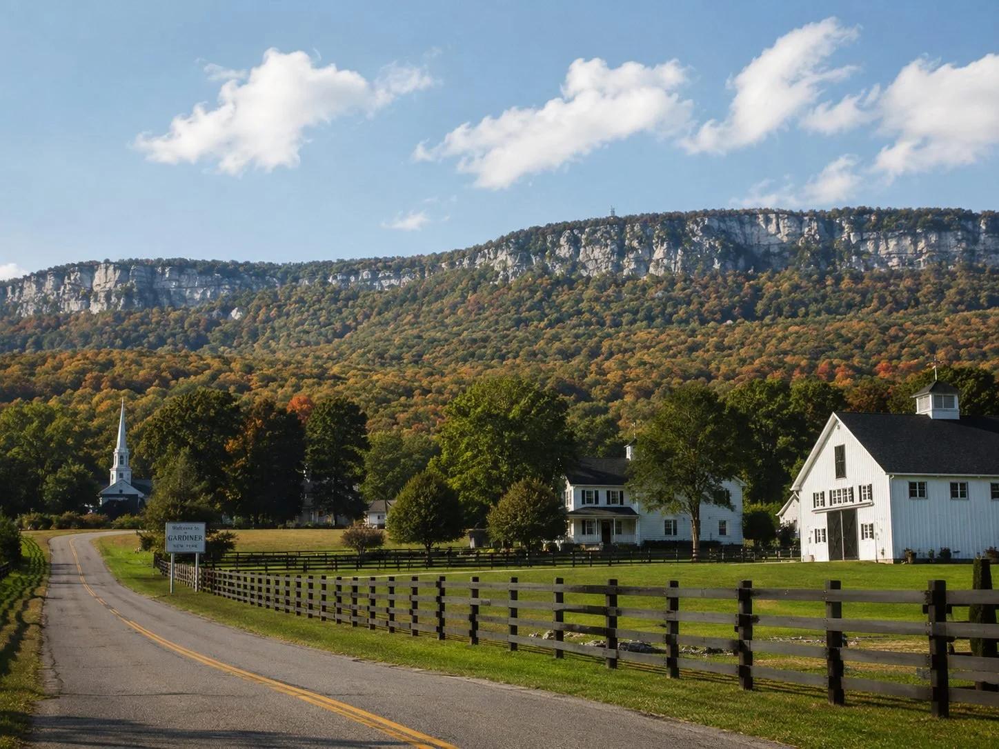 Gardiner, NY rural road with farm fields, a white barn, village buildings, and the Shawangunk Ridge in the background.
