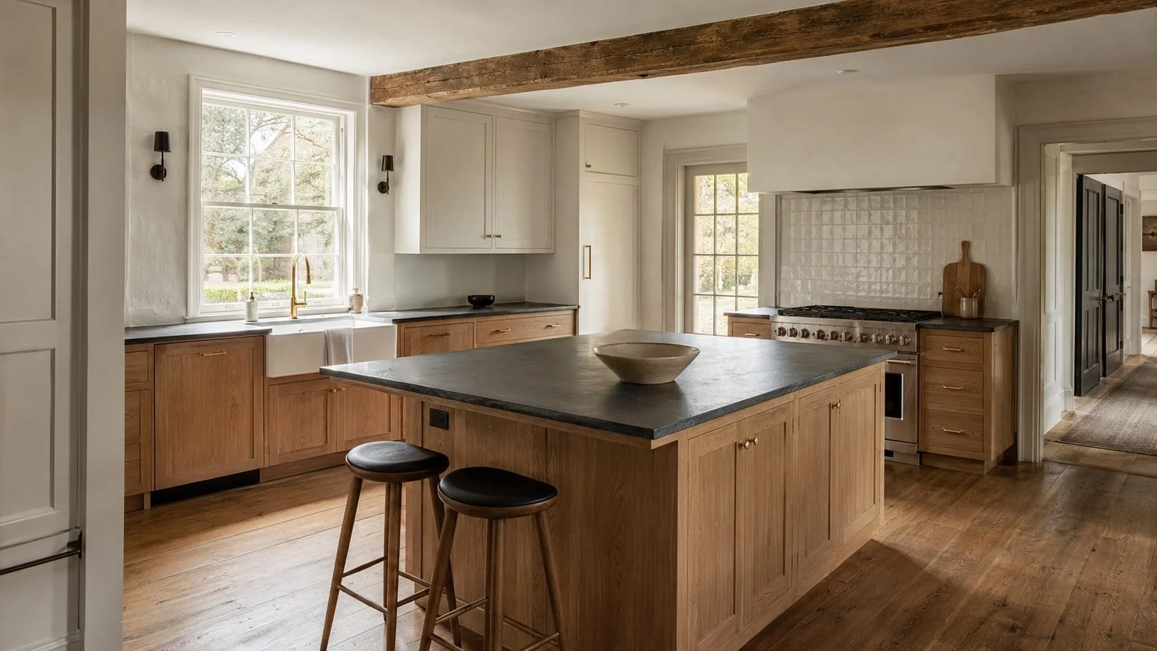 Farmhouse kitchen with white oak cabinets, dark stone island, apron-front sink and exposed timber beam