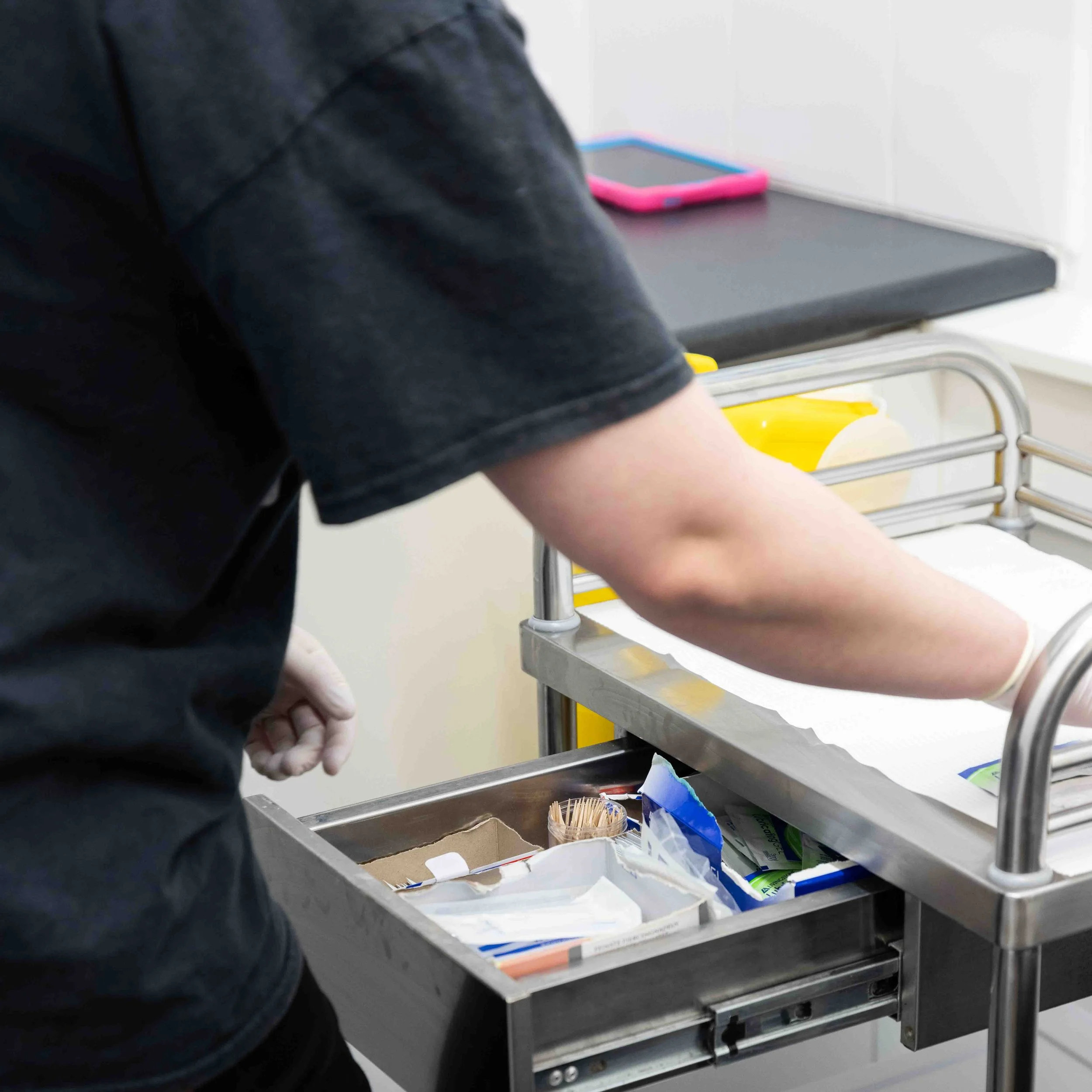 A healthcare worker pushing a medical cart with supplies, including gloves and bandages, in a clinical setting.