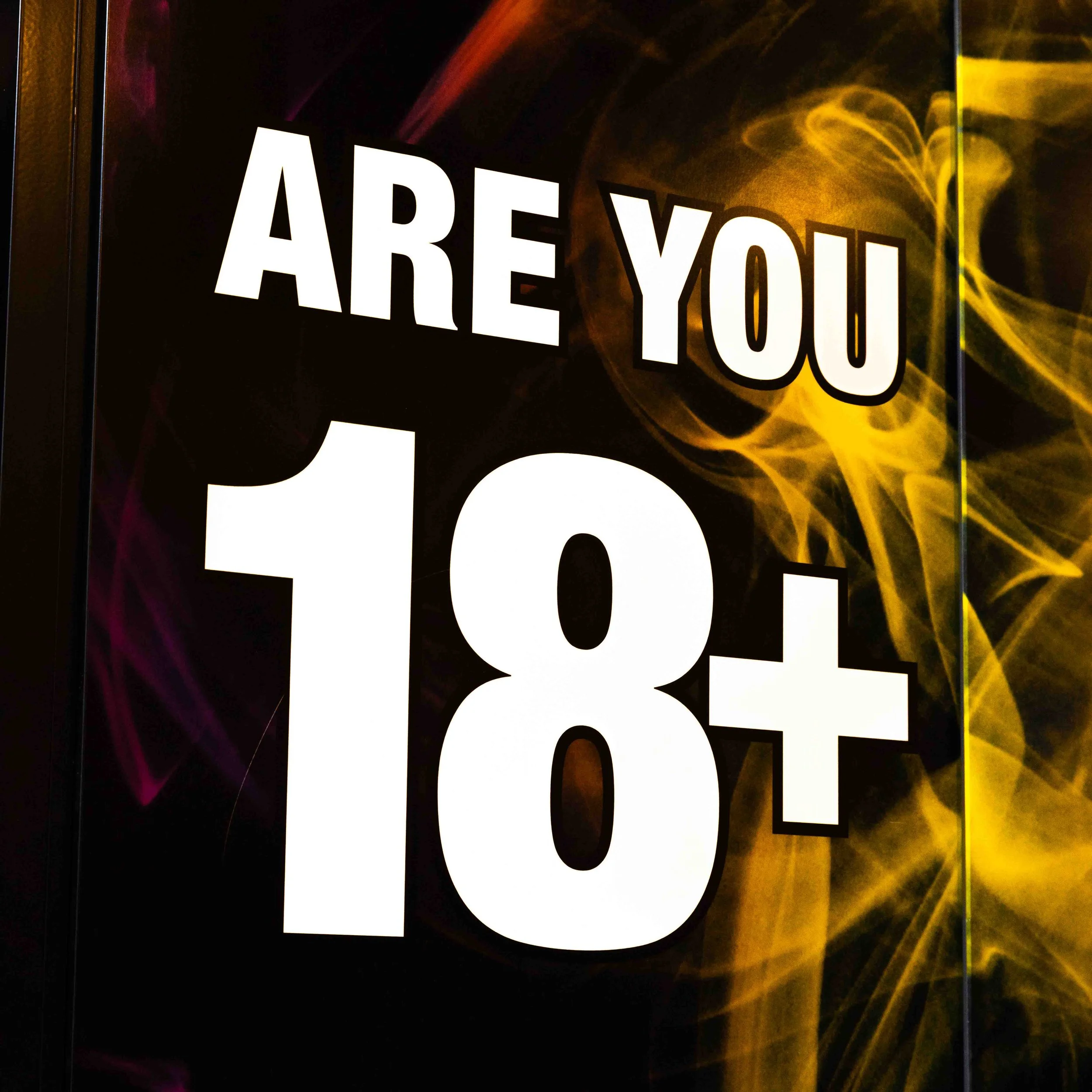 Sign with the text "ARE YOU 18+" in bold letters, with a black background and yellow smoke-like design.