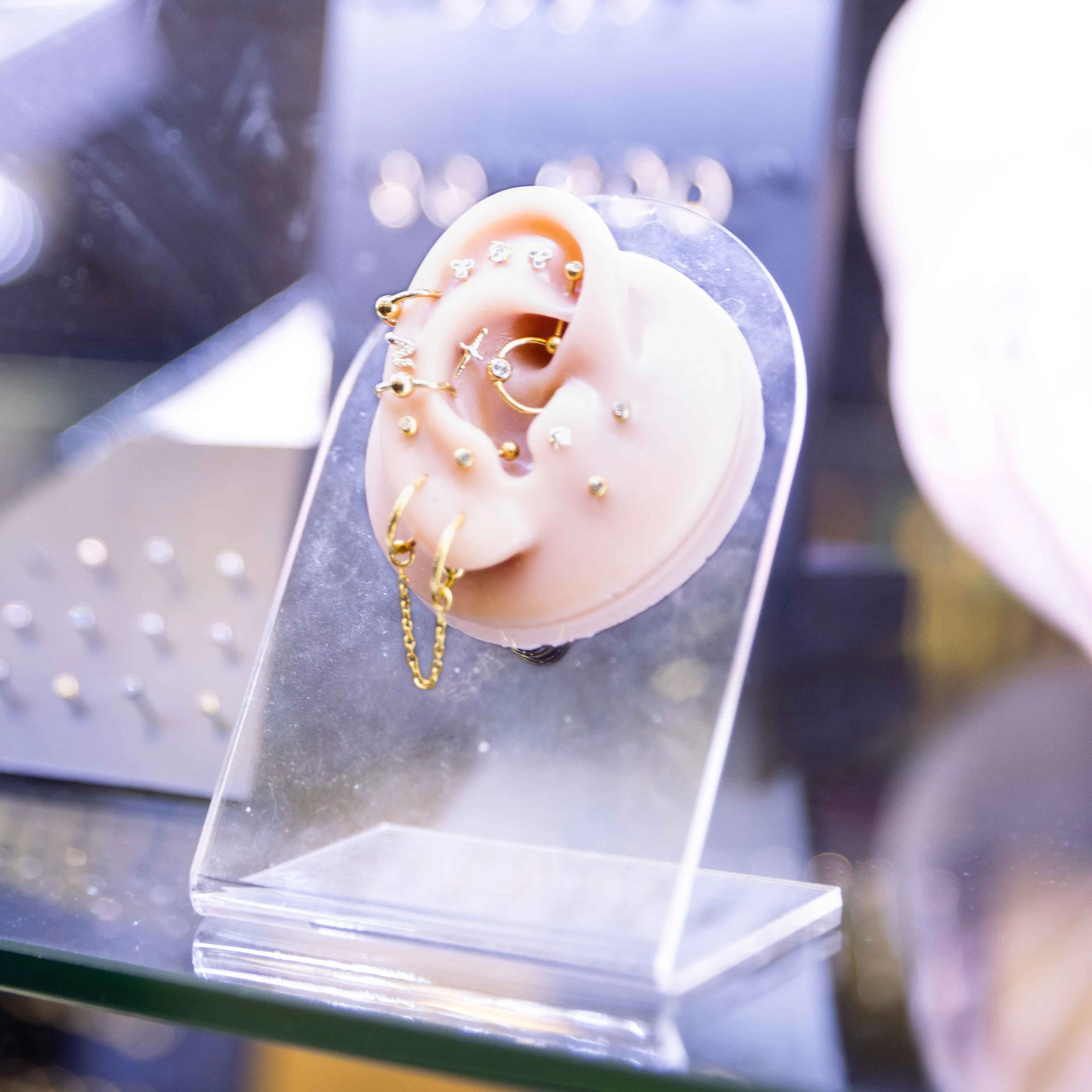 An earlobe-shaped display with various gold and diamond earrings on a clear stand.
