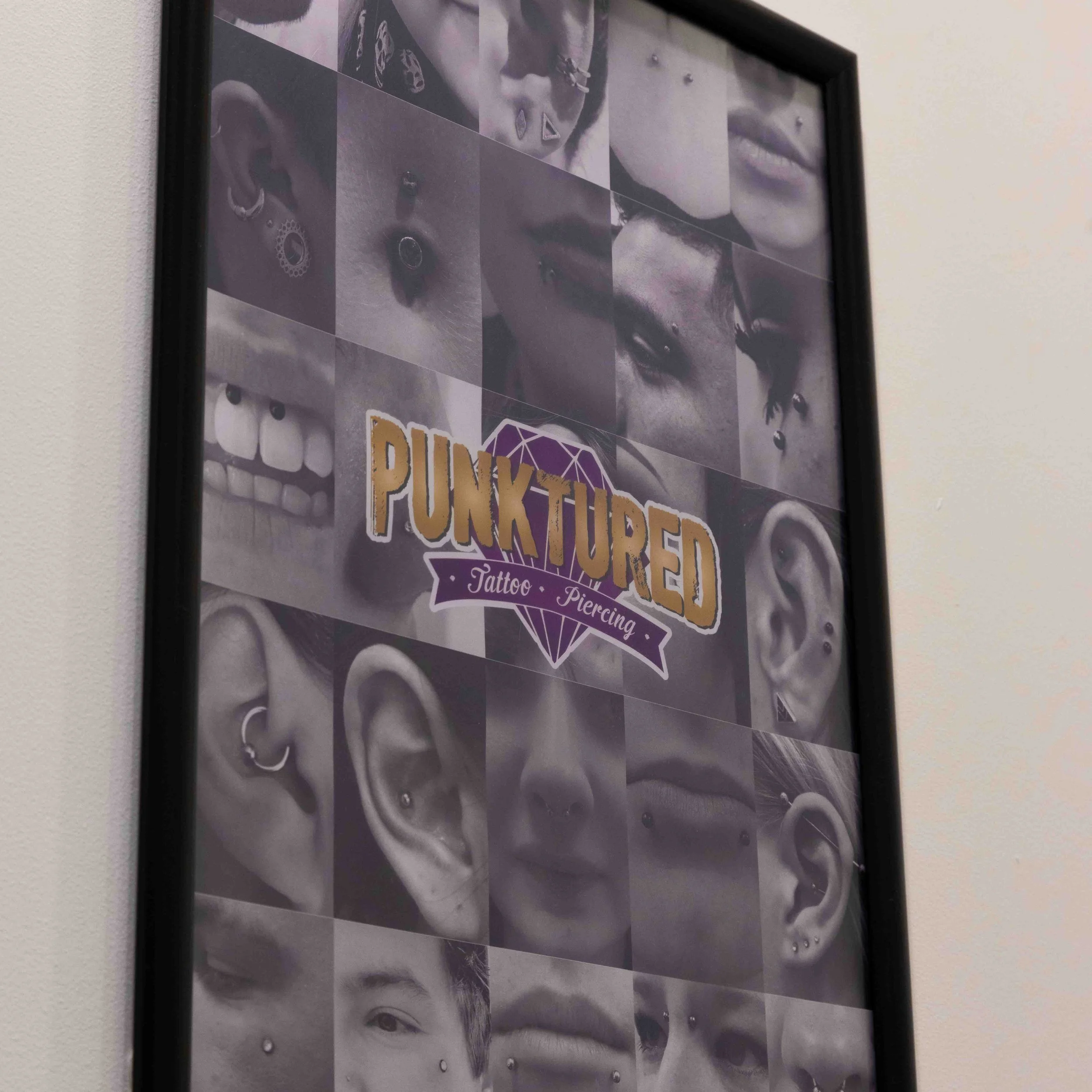 Framed poster advertising a tattoo and piercing studio called PunkTured, featuring black and white photos of various facial piercings and tattoos.
