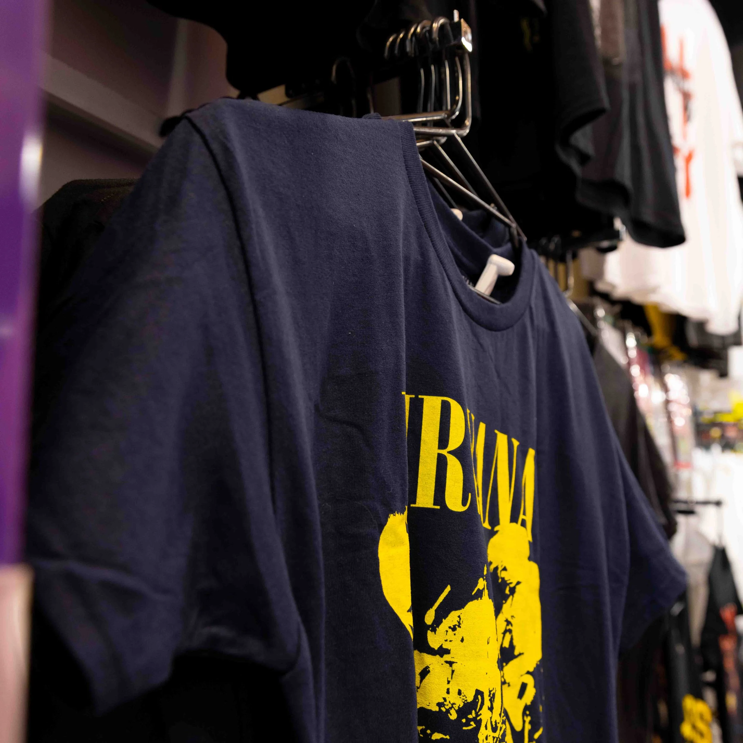 Blue T-shirt with yellow graphic and text hanging on a rack in a clothing store.