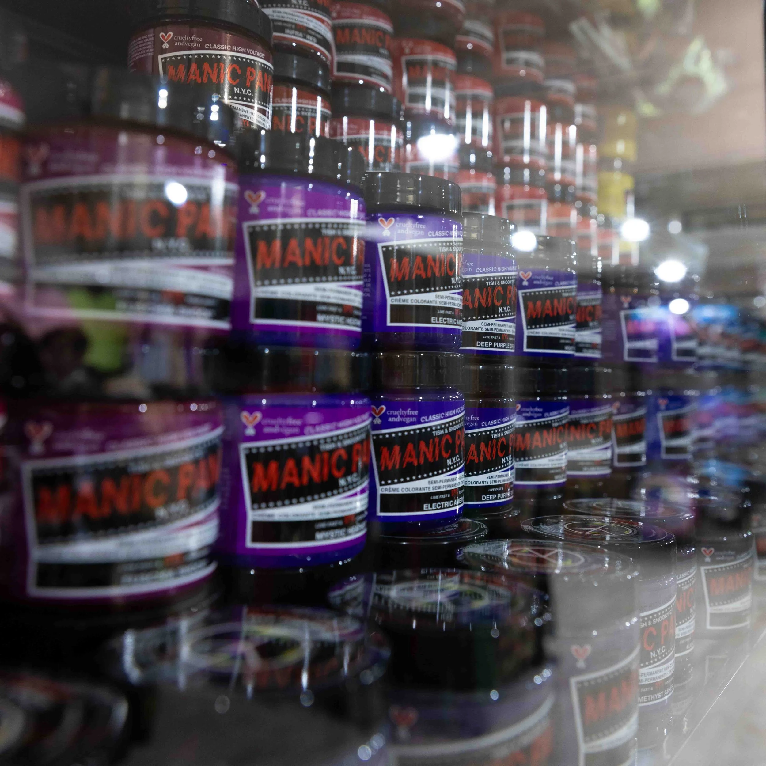 Rows of colorful hair dye containers labeled 'Manic Panic' on store shelves, with some reflecting off the glass surface.