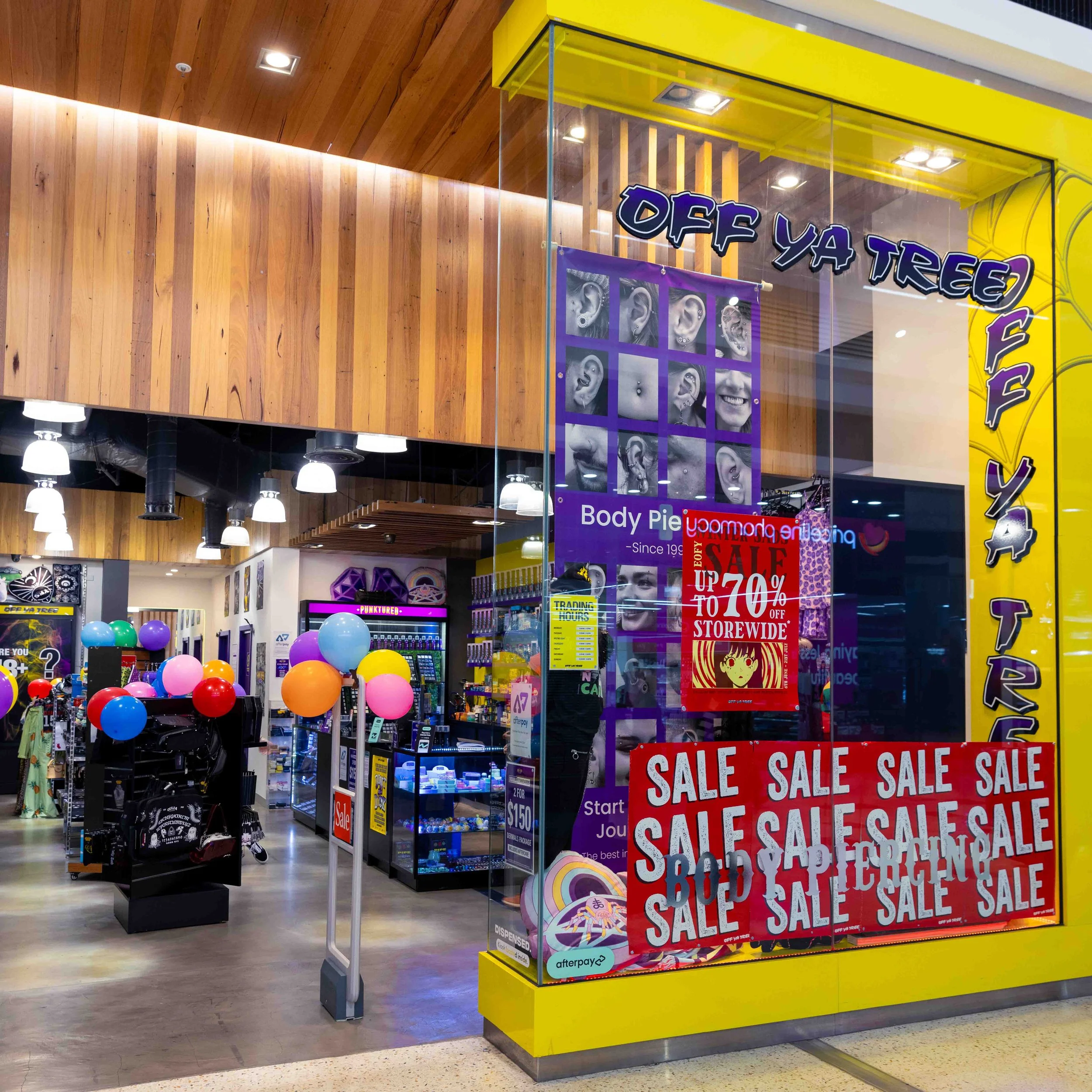 Storefront with yellow framing and sale signs in a retail store featuring balloons and merchandise displays inside.
