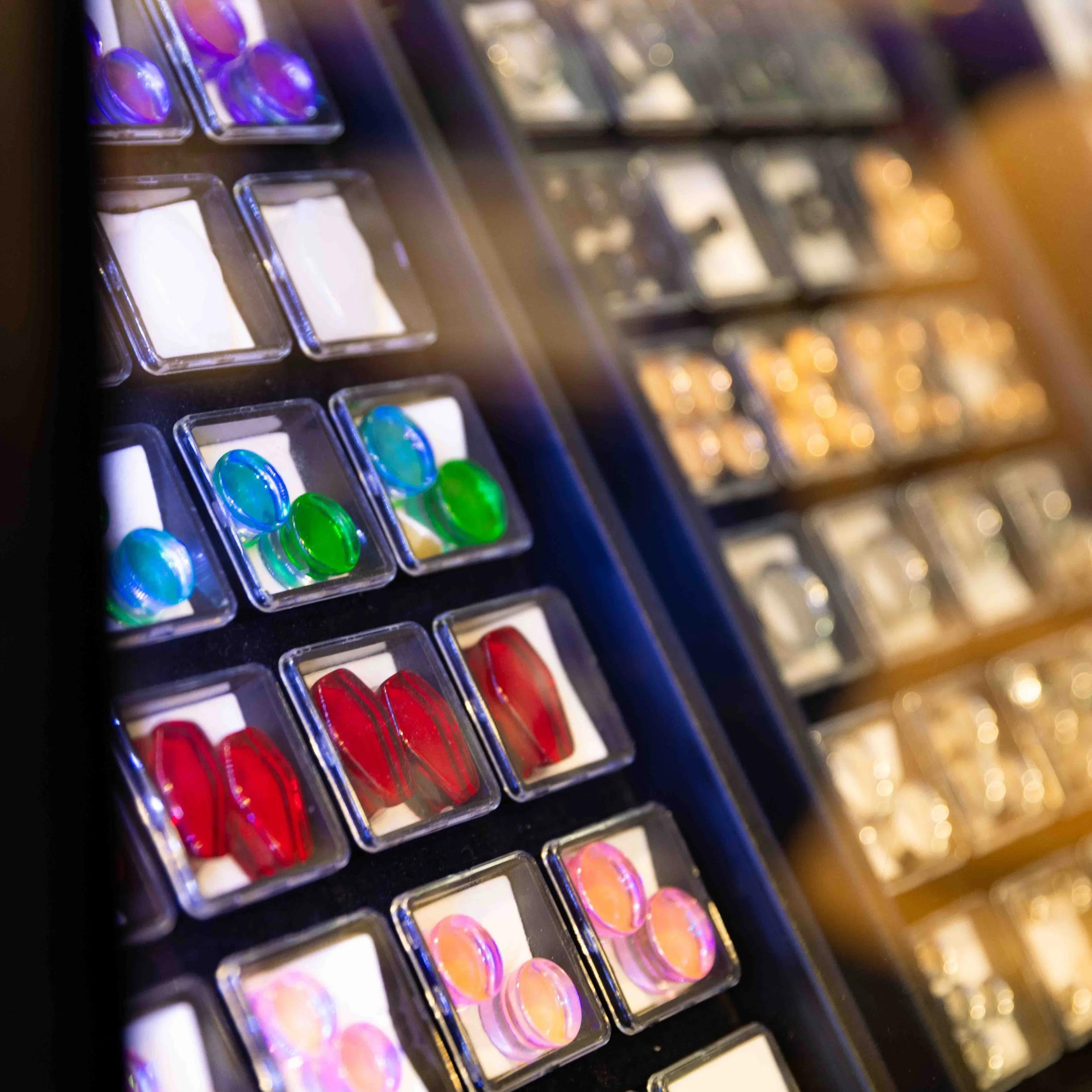Close-up of a display case with colorful, shiny glass or plastic cabochons in various sizes and colors, including blue, green, red, and pink.