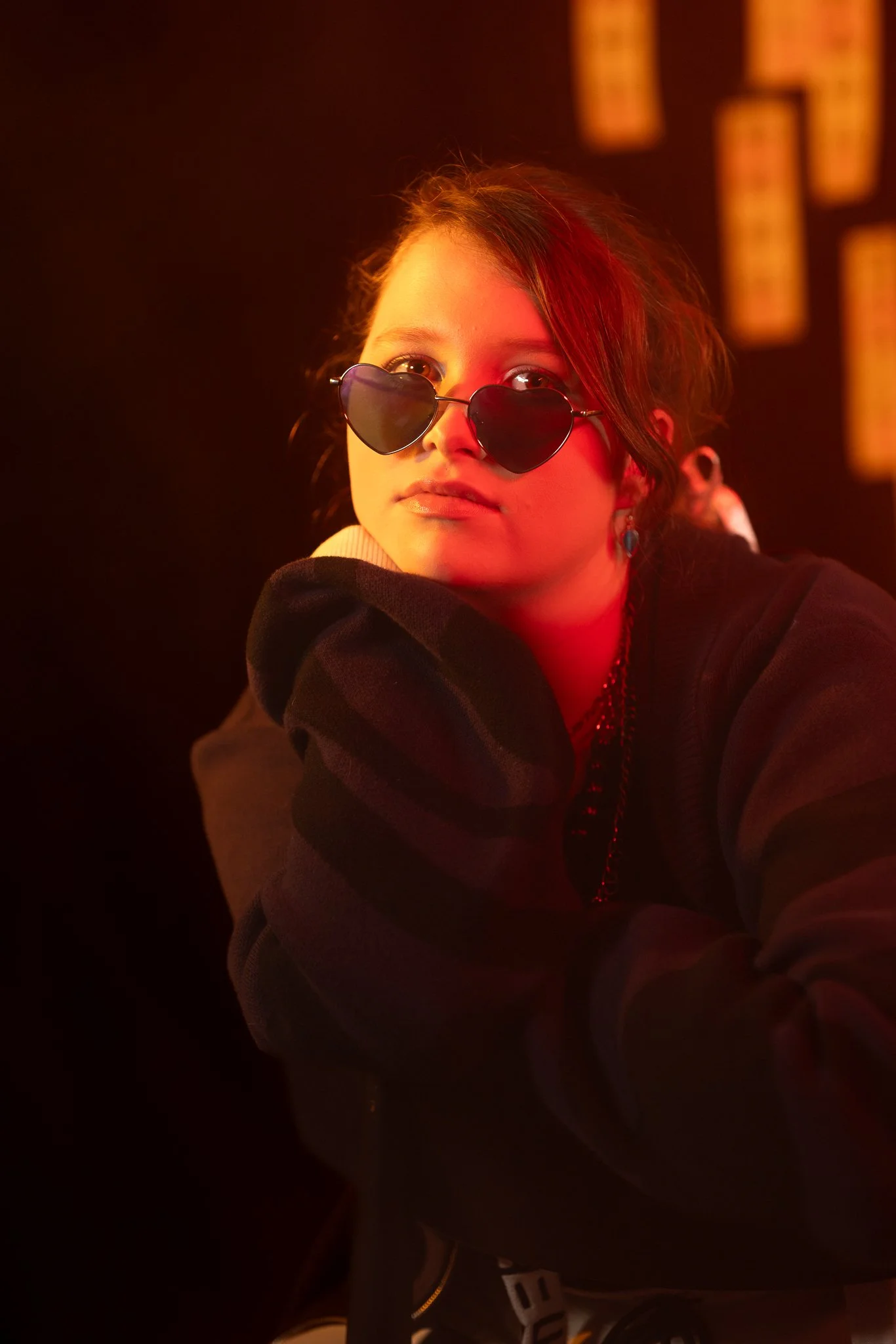 A young woman with heart-shaped sunglasses glowing in red light.