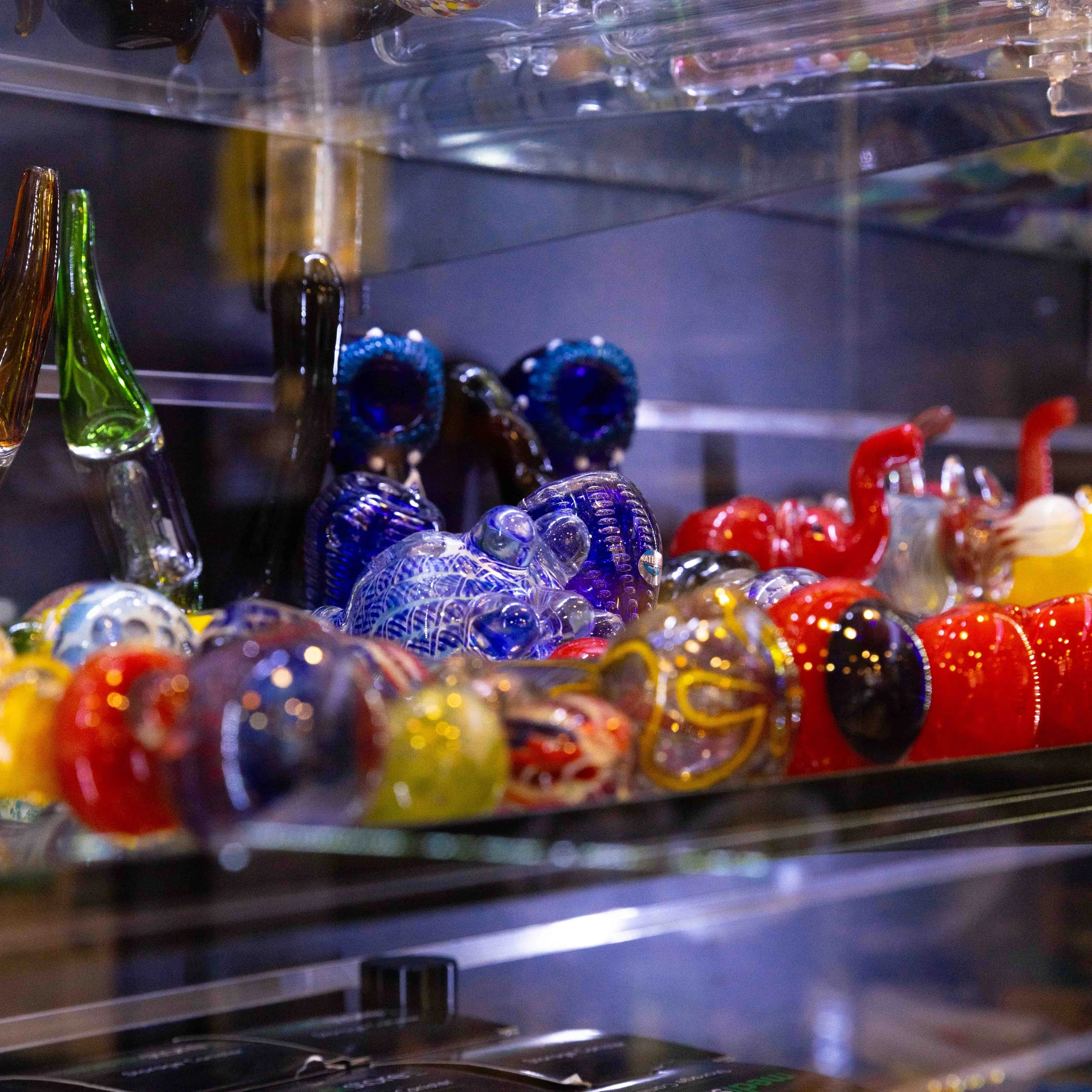 A display case filled with colorful glass art sculptures, including various animals and abstract shapes in blue, red, yellow, and green.