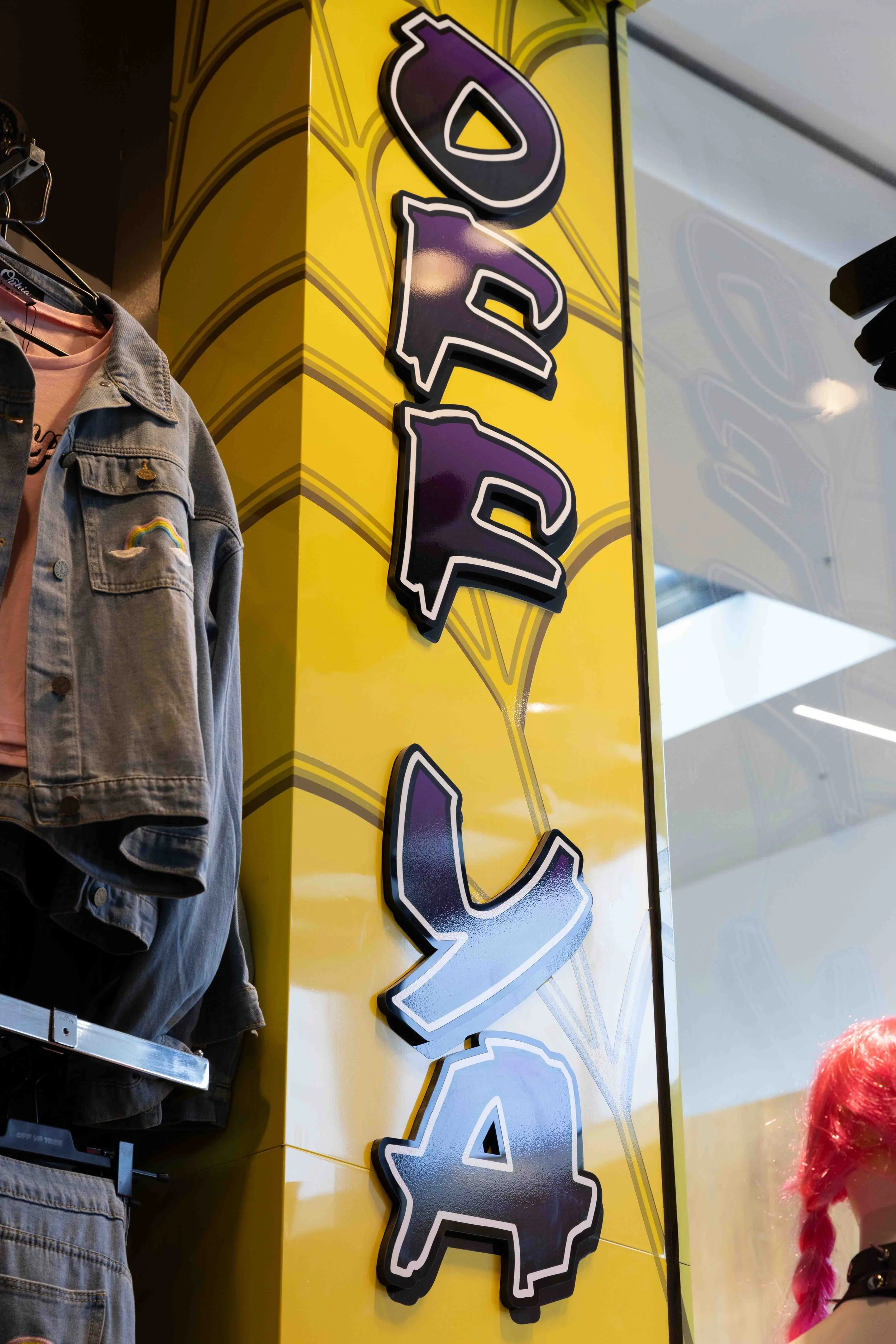 Sign that reads 'POP PARADISE' in colorful 3D letters inside a store with clothing on display.
