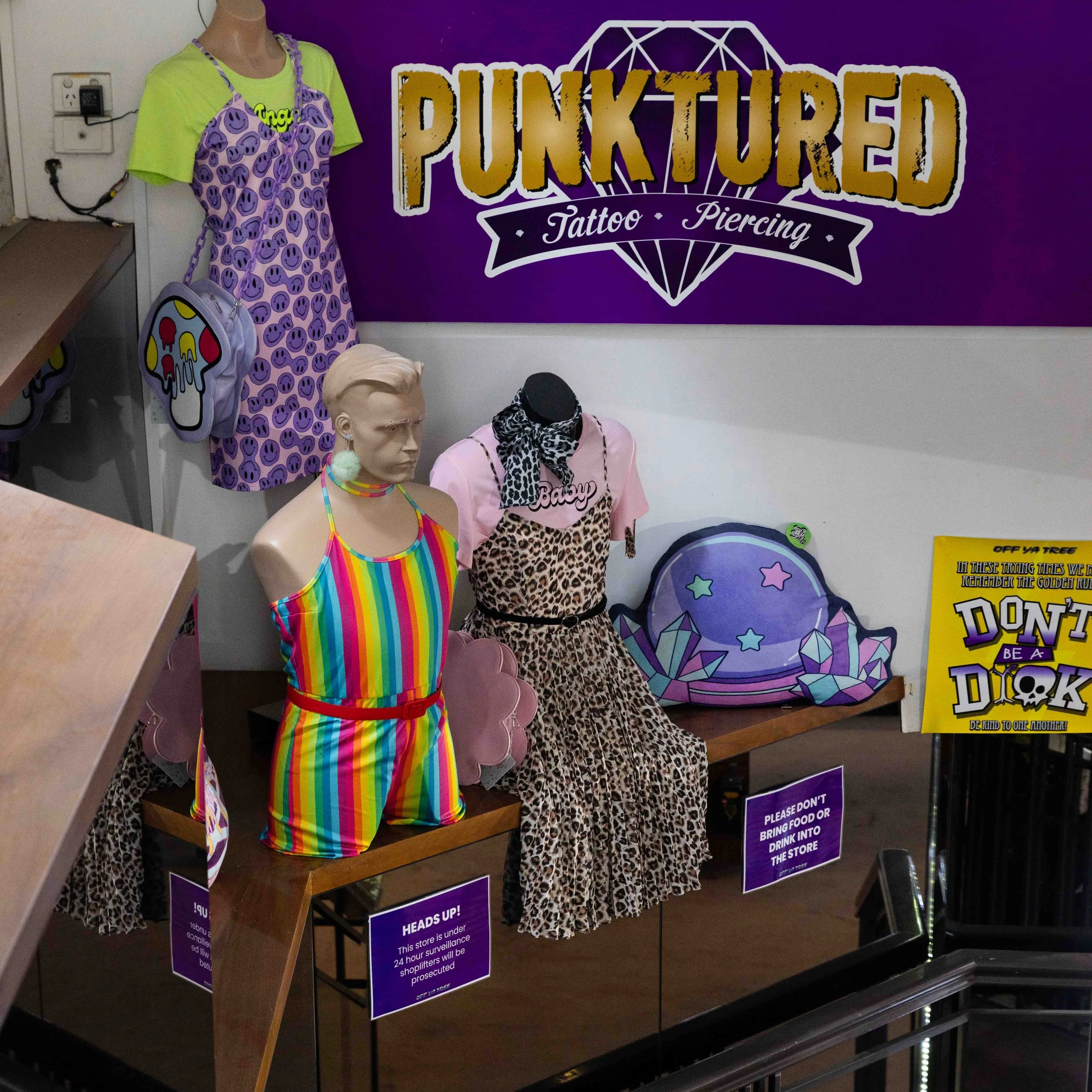 Display of colorful mannequins with punk-inspired fashion accessories and clothing, positioned in front of a purple sign reading 'PUNKTURED Tattoo Piercing.'
