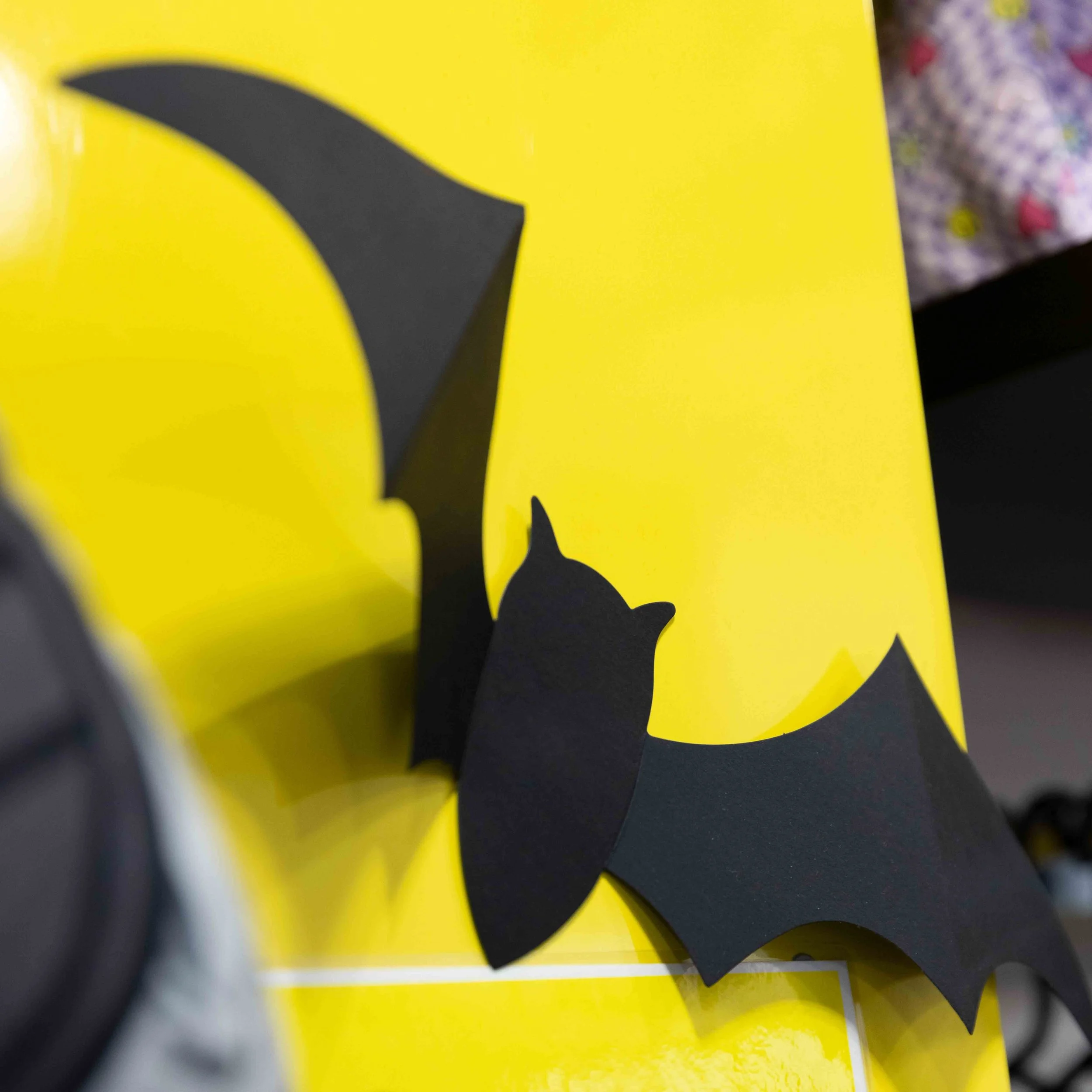 Black paper cutout of bats attached to a yellow surface.