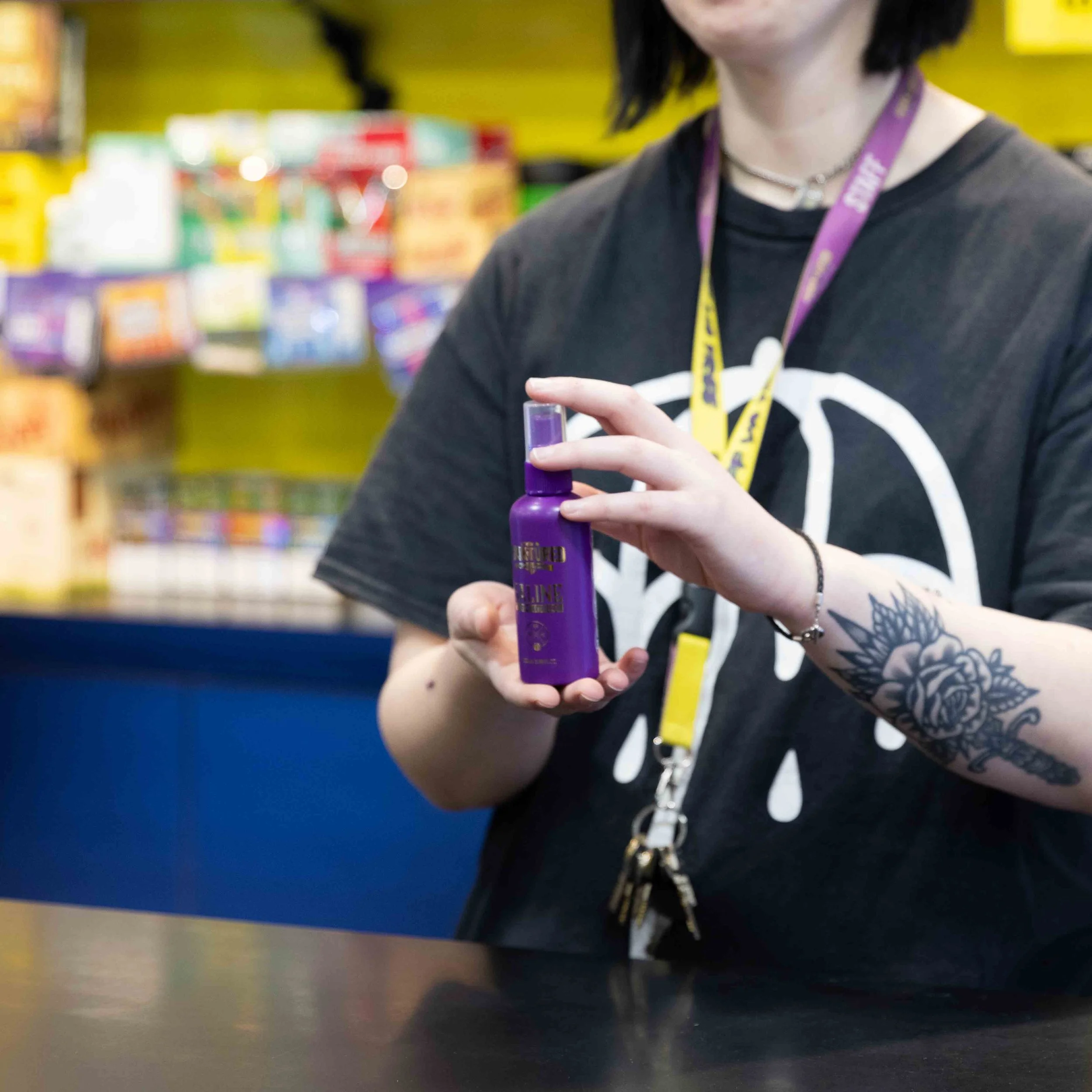 A person holding a purple spray bottle in a retail store, with colorful products on store shelves in the background.