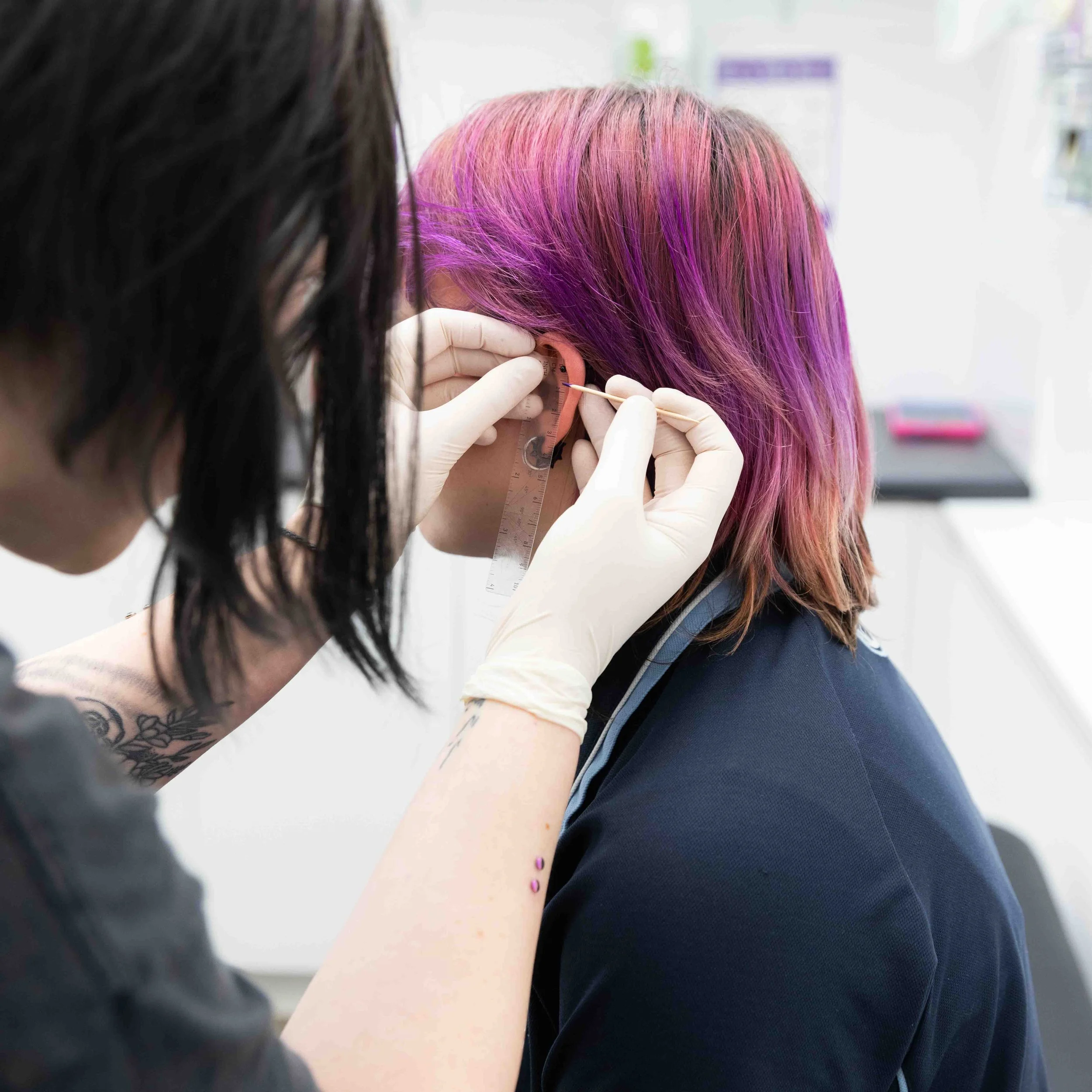 A person with multicolored pink and purple hair getting an ear piercing at a clinic.