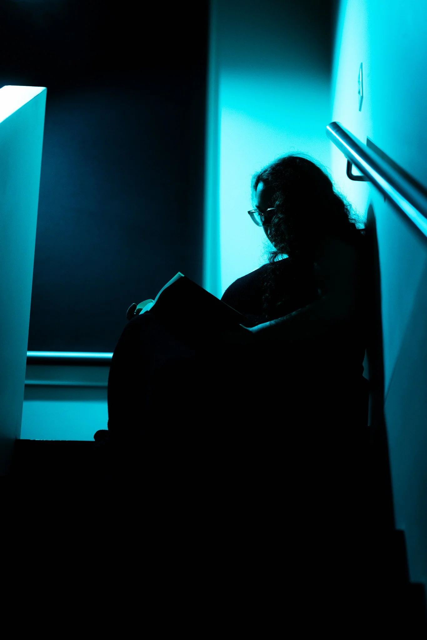 Silhouette of a person sitting on stairs, reading a book, illuminated by blue lighting