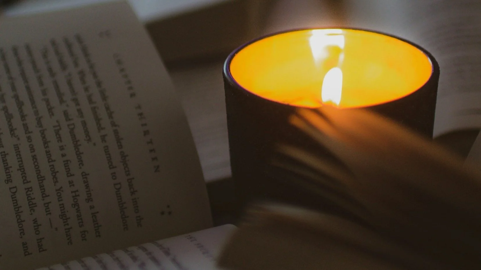A lit candle inside a black holder on an open book with visible text.