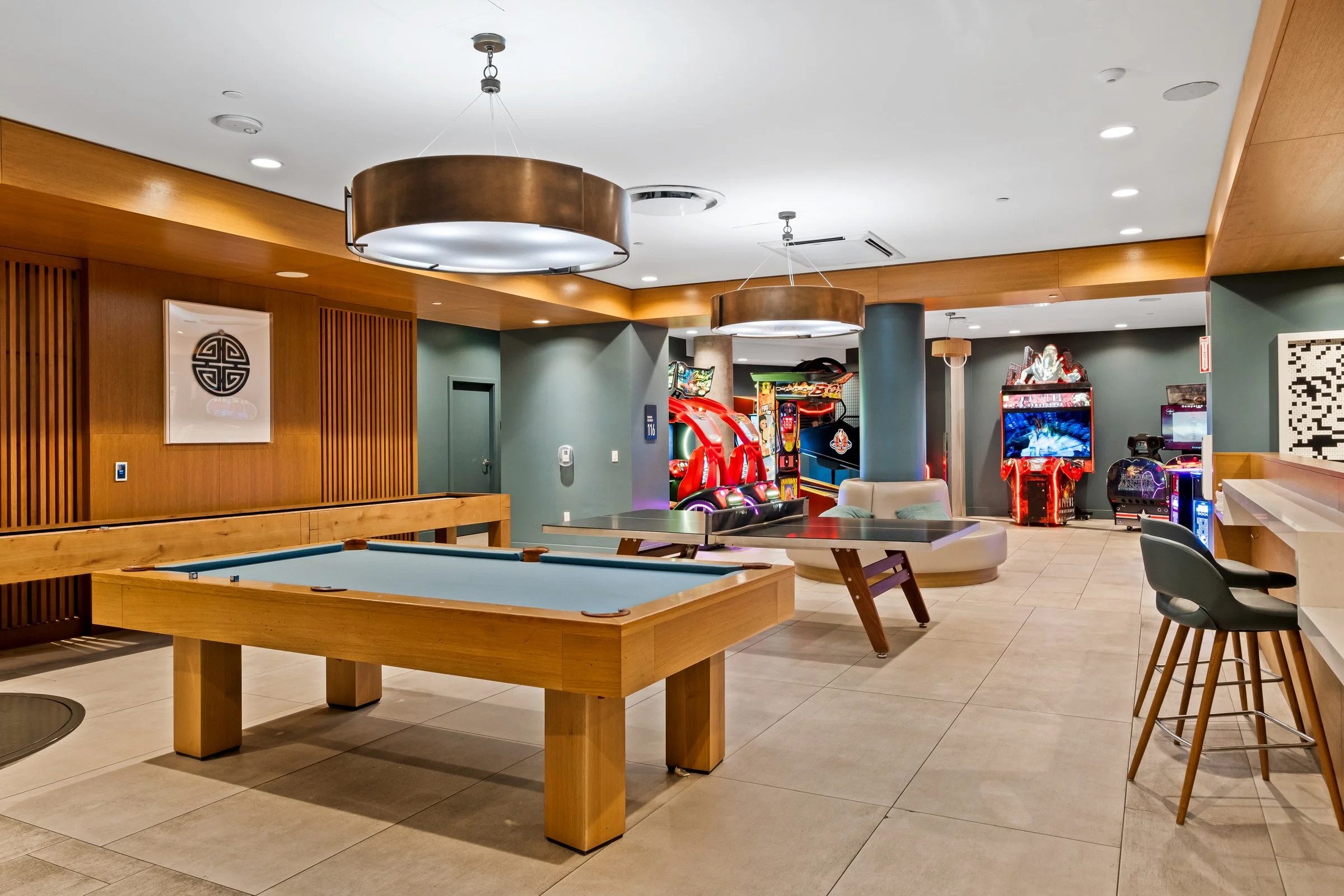 Indoor entertainment lounge featuring a pool table, arcade games, seating area, and bar stools.