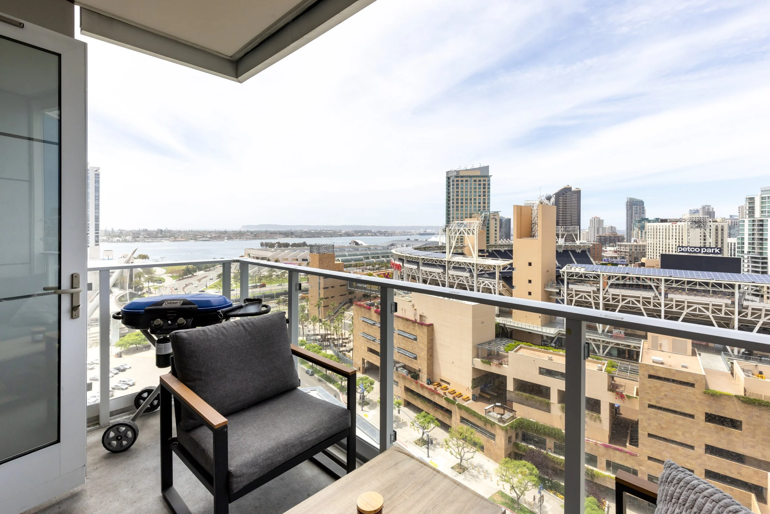 Balcony with outdoor furniture, view of a city skyline, stadium, water, and a bridge in the background.