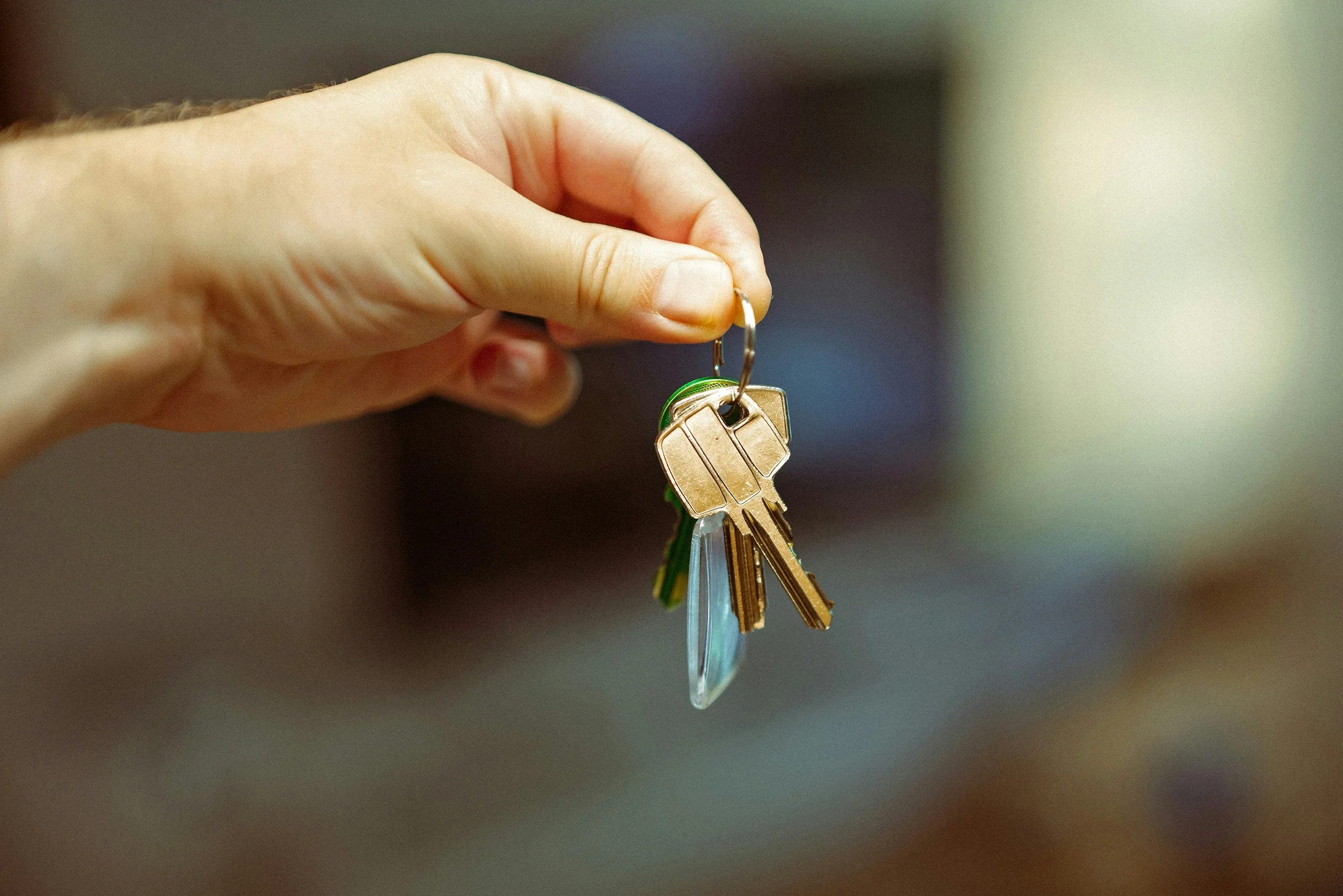 A hand holding a keychain with several keys, including a clear plastic key, a green key, and a gold key.