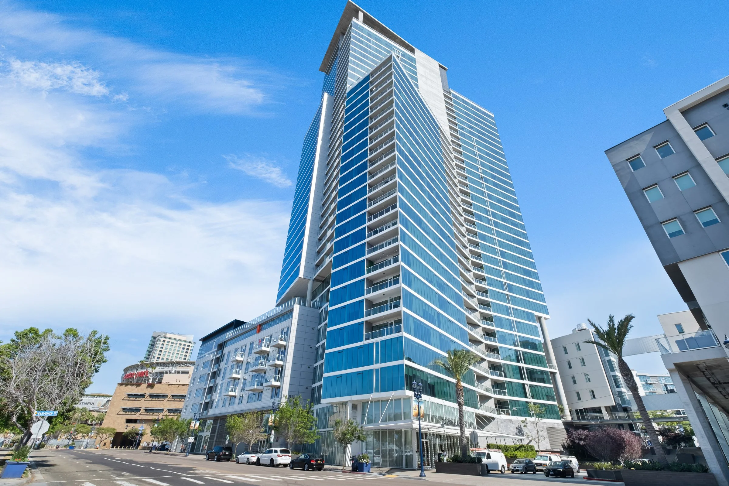 Modern glass skyscraper in downtown with palm trees and parked cars in foreground
