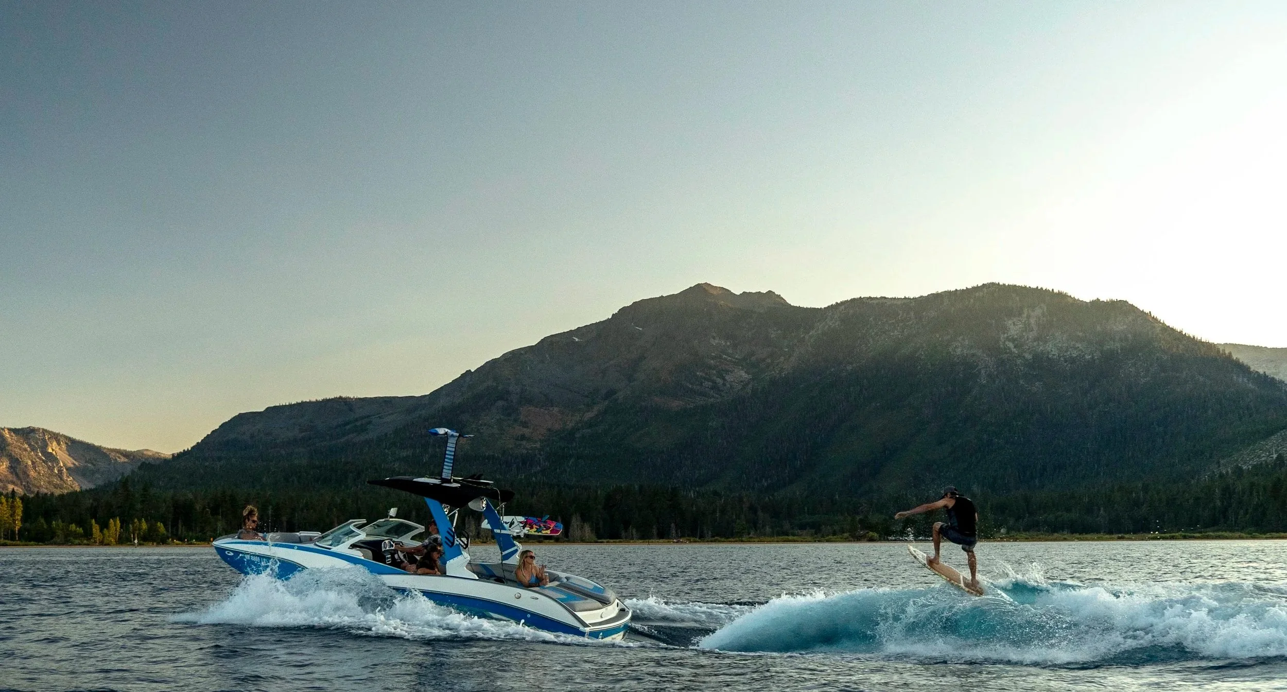 People enjoying water activities on a lake with a mountain in the background, including a speedboat and a person wakeboarding.