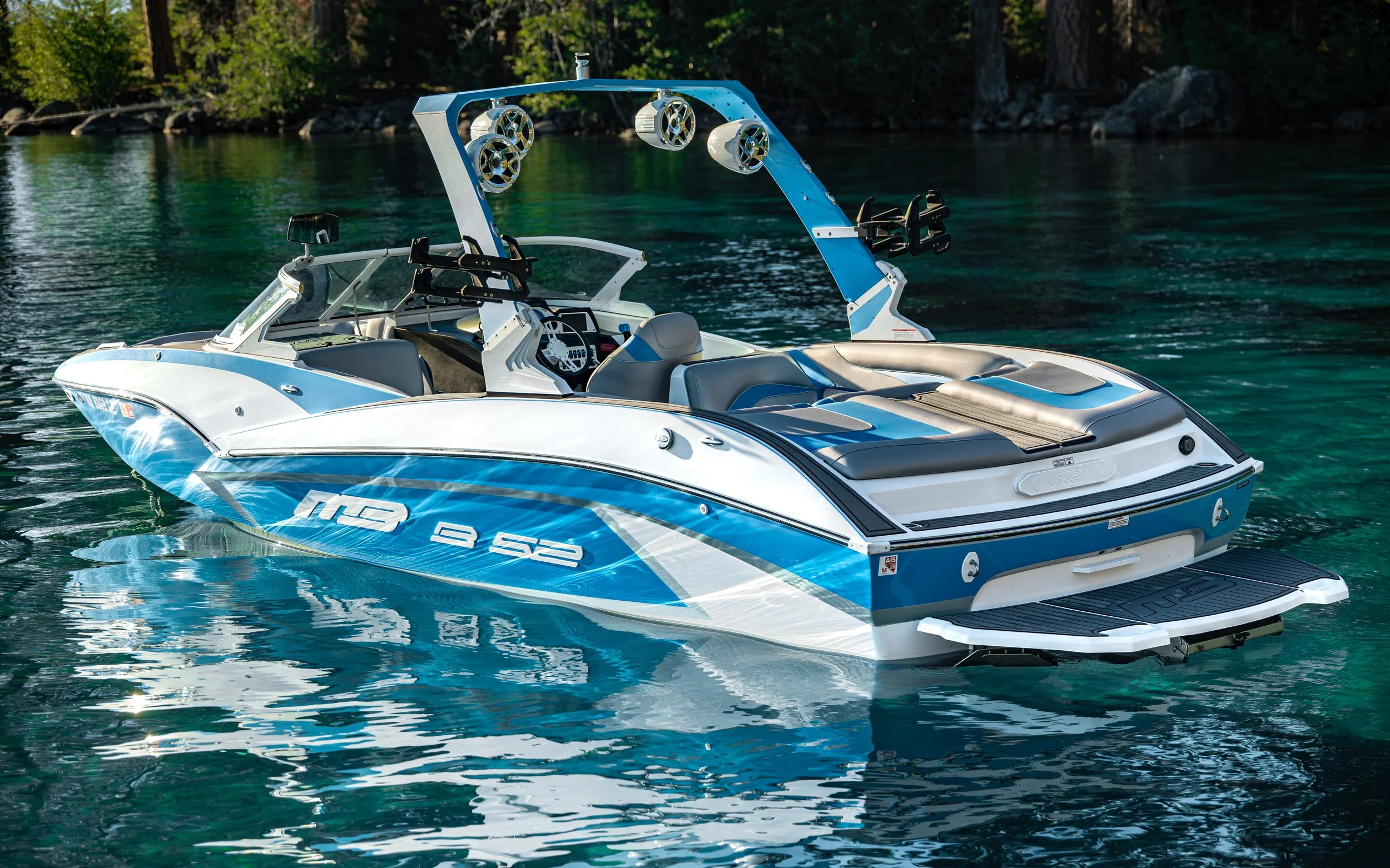 A blue and white speedboat floating on clear green water with a forested shoreline in the background.