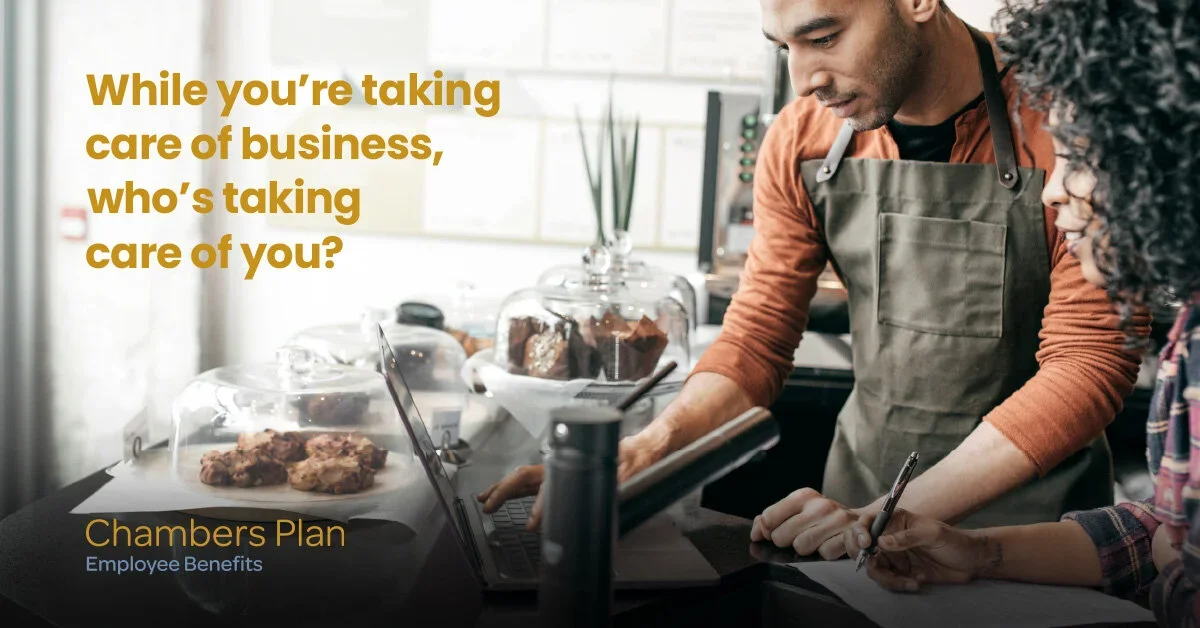 Two people working at a counter with baked goods, one using a laptop and the other taking notes.