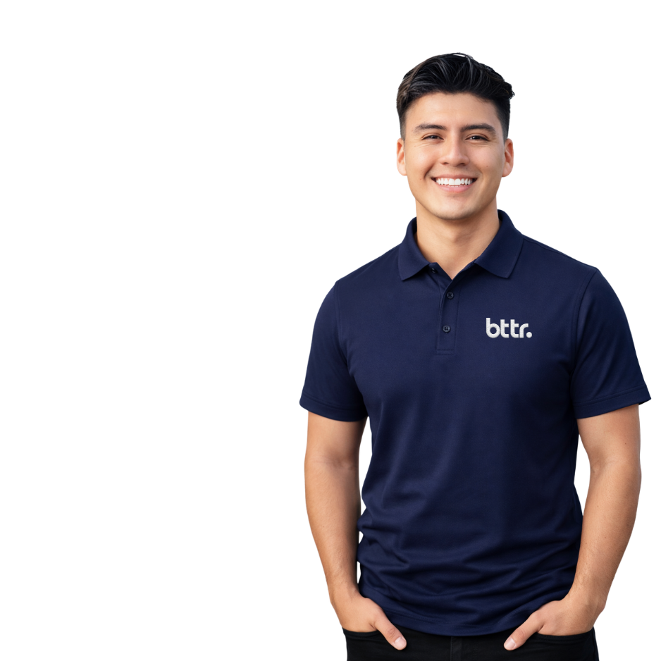 A young man with dark hair and light skin wearing a navy blue polo shirt with 'bttr.' logo smiling with hands in pockets.