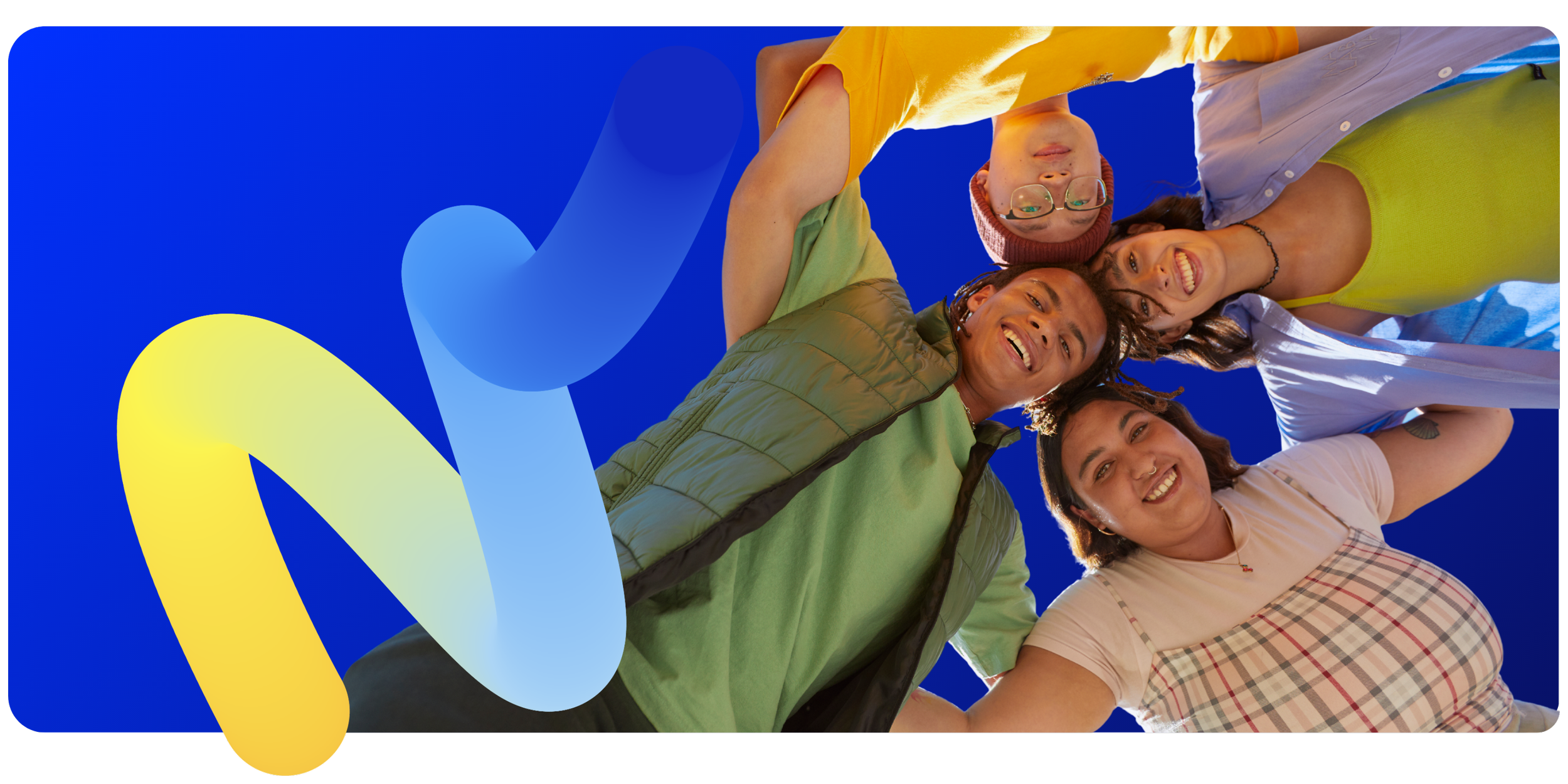 Group of five diverse young adults smiling and lying close together outdoors against a bright blue sky background.
