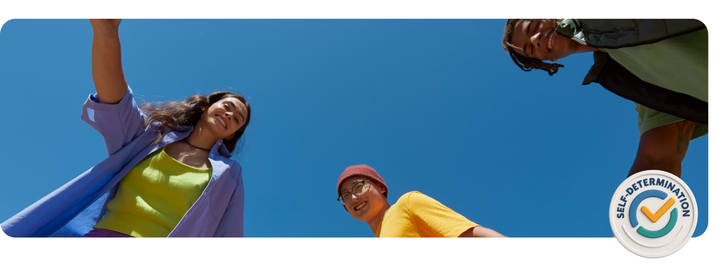 Three young people smiling and looking down at the camera, against a clear blue sky. One woman wearing a purple shirt and yellow top, one man wearing a yellow shirt and red beanie, and another man in a green shirt and black jacket. There is a logo with a check mark and the text 'Self-Determination' in the bottom right corner.