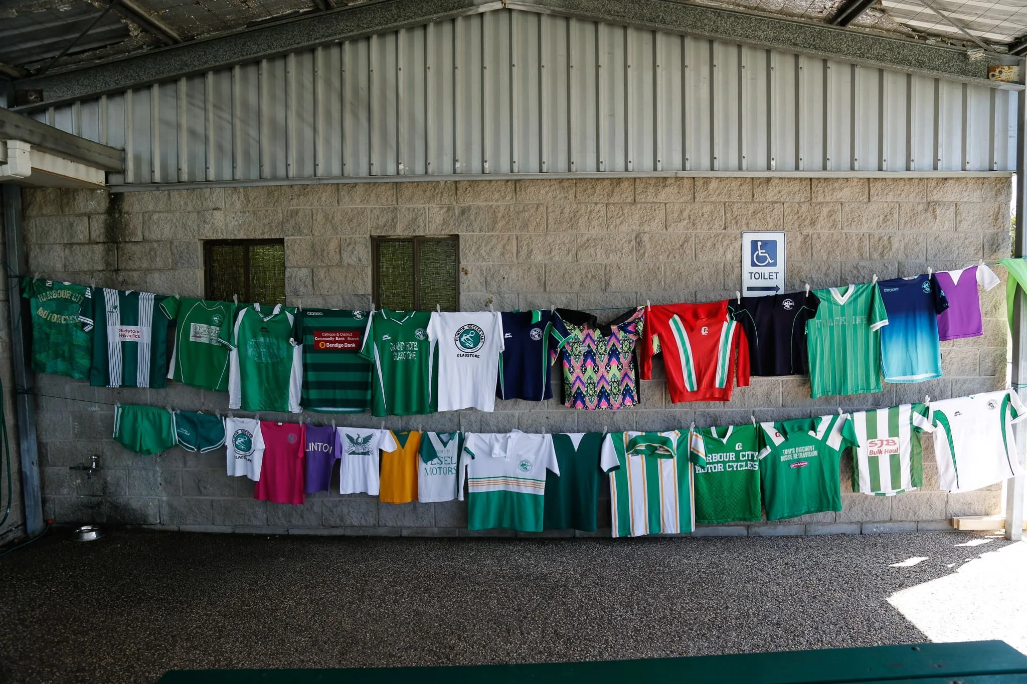 Clothesline with sports jerseys hung to dry in front of a brick wall, with a wheelchair accessible toilet sign on the wall.