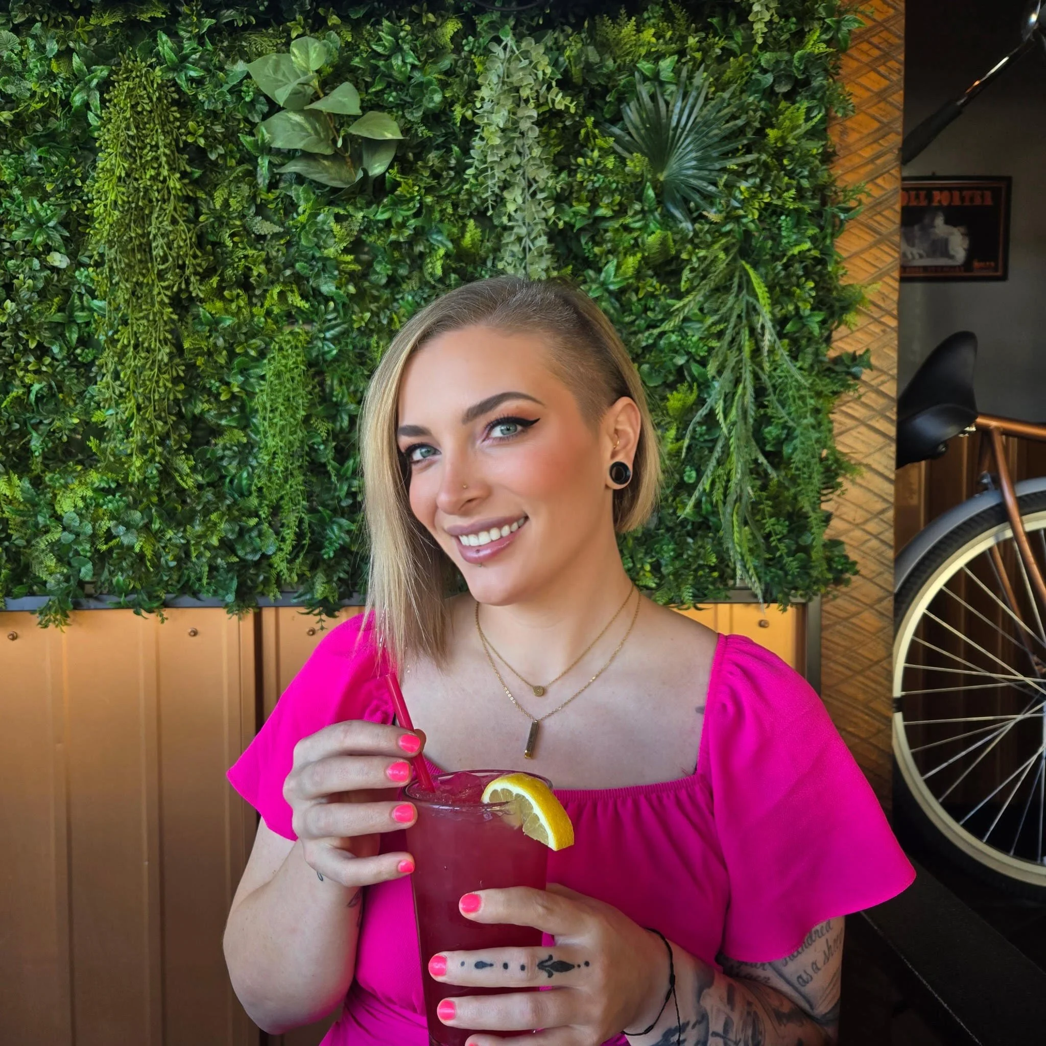 PR Team Member in a pink dress, sitting in a restaurant with a drink in hand.