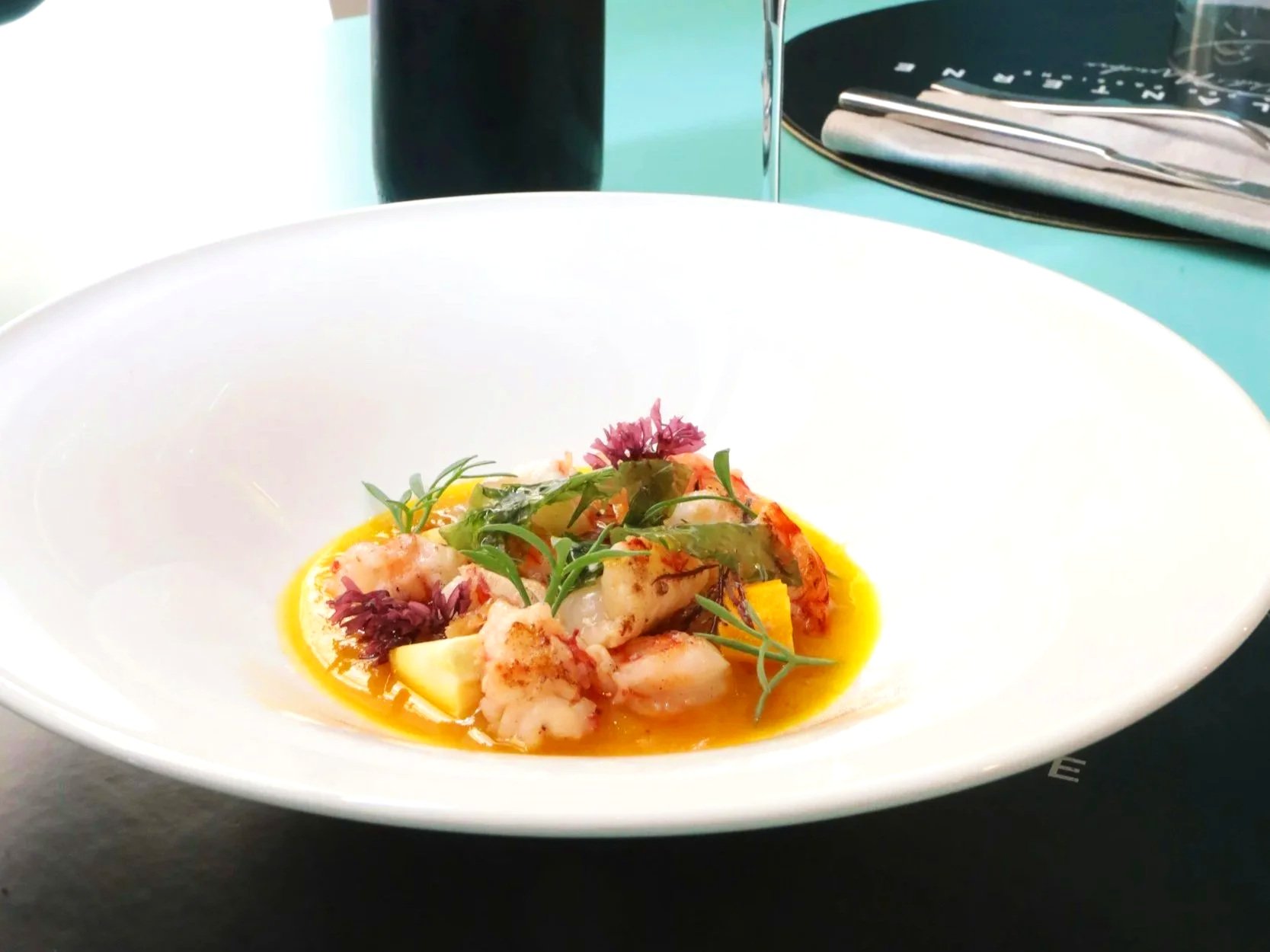 Seafood dish featuring shrimp, a poached egg, microgreens, and a biscuit topped with caviar on a white plate