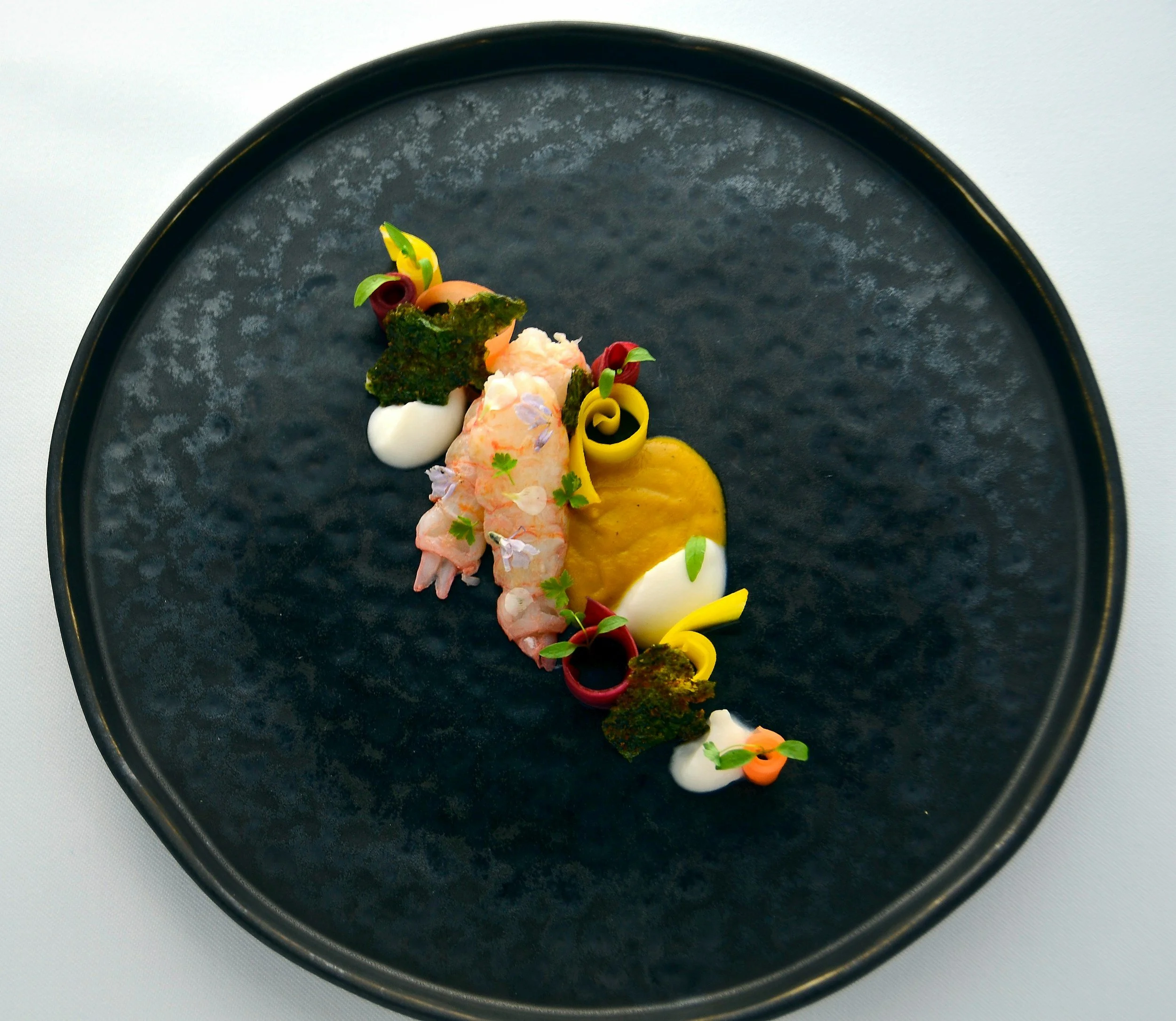 Seafood dish featuring shrimp, a poached egg, microgreens, and a biscuit topped with caviar on a white plate