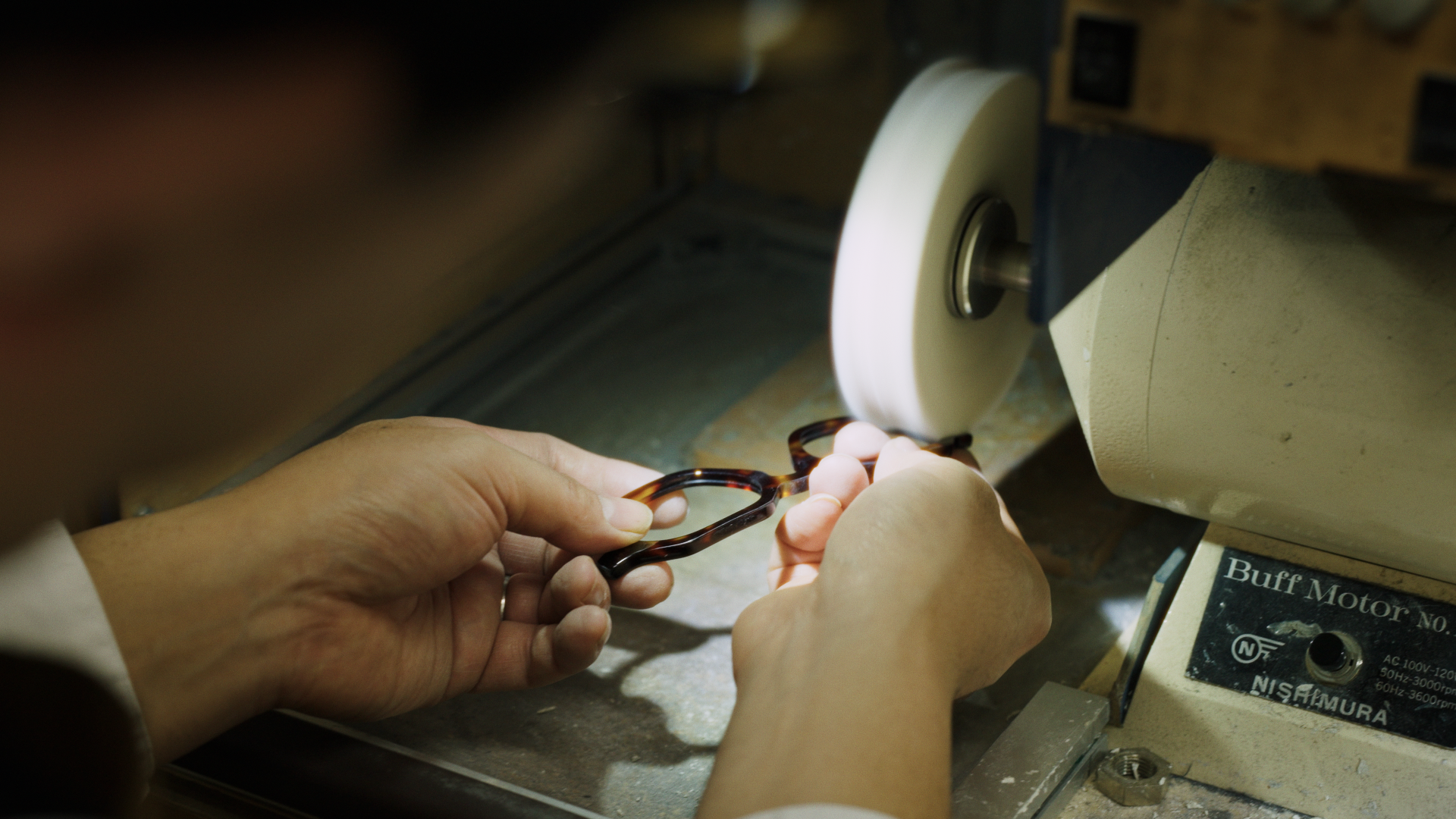 Person polishing eyeglasses on a buffing machine in a workshop.