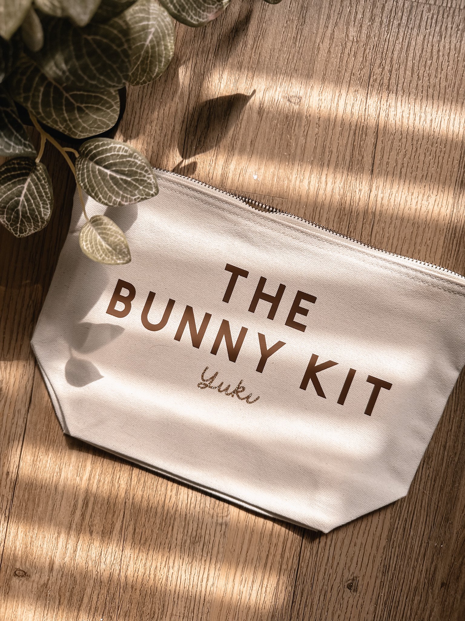 Trousse de soins pour bébés, nommée "The Bunny Kit" avec le nom "Louka" écrit en cursif, posée sur une surface en bois avec une plante verte à côté.