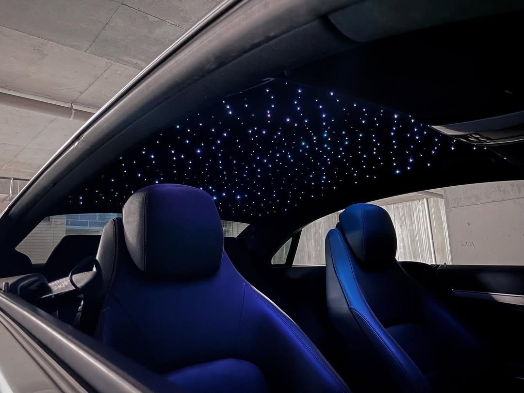Interior of a car showing black leather seats and a ceiling with blue LED star lights.