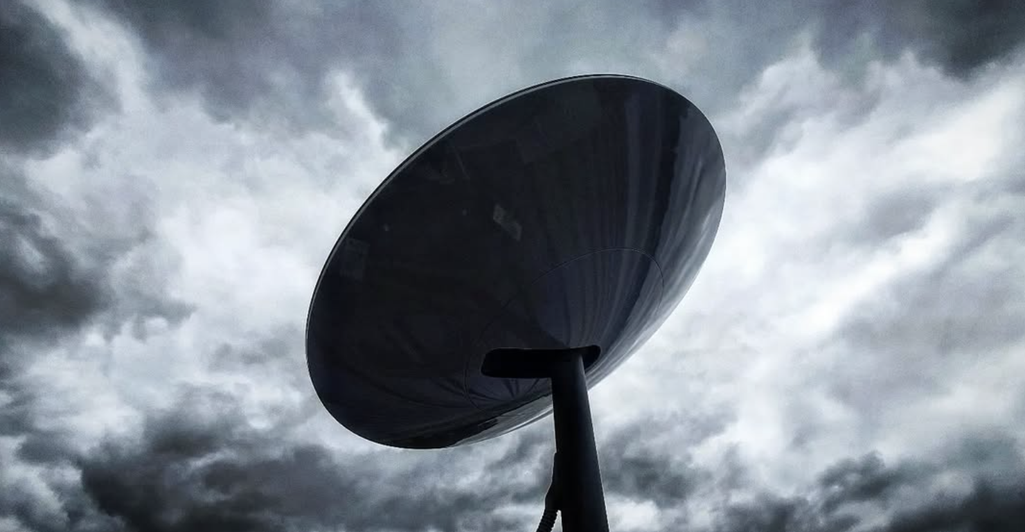 A large, dark, futuristic umbrella-like structure with a tall support stand against a cloudy, overcast sky. Starlink wifi internet network