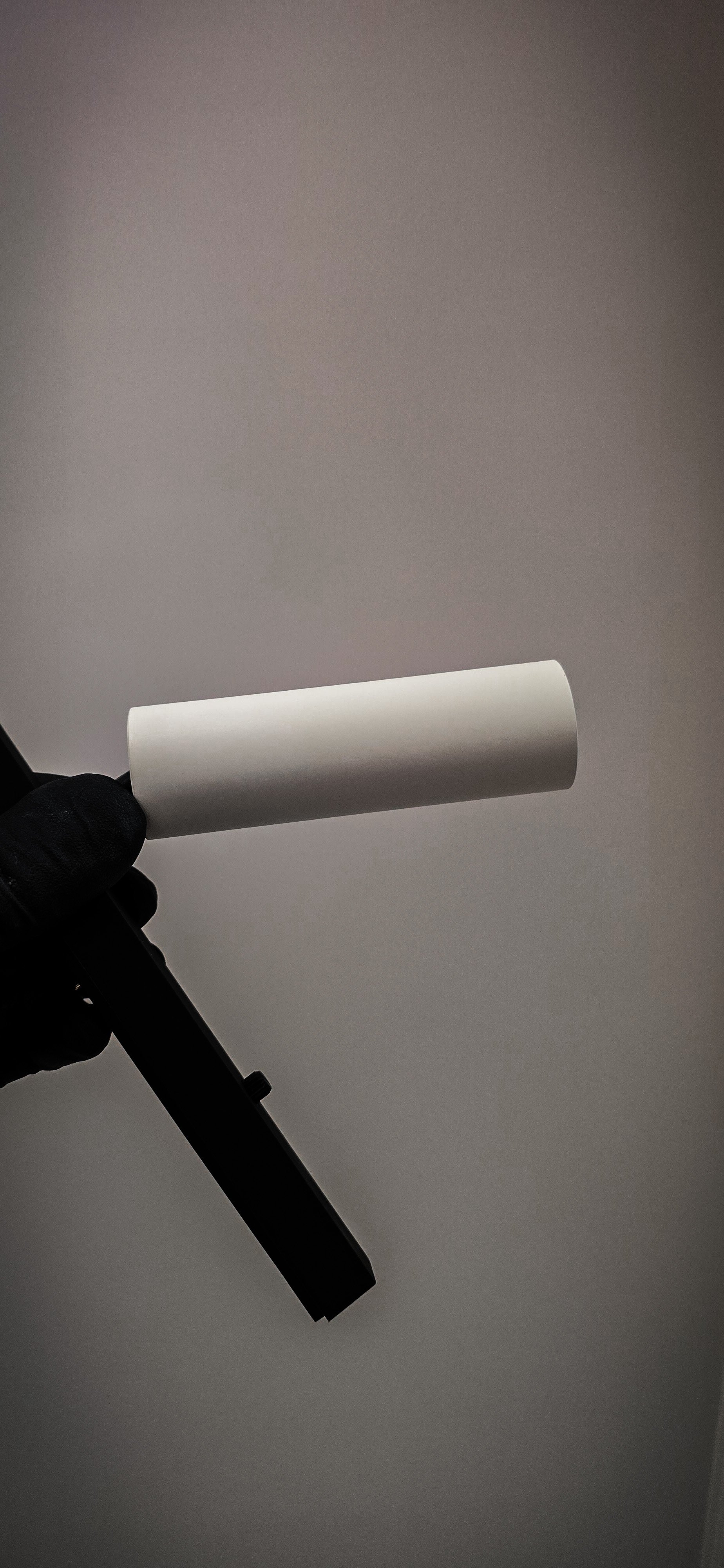A hand in a black glove holding a squeegee with a white cylindrical object attached, against a plain, light gray background. Track lighting, downlight, electrical light repair, custom lighting