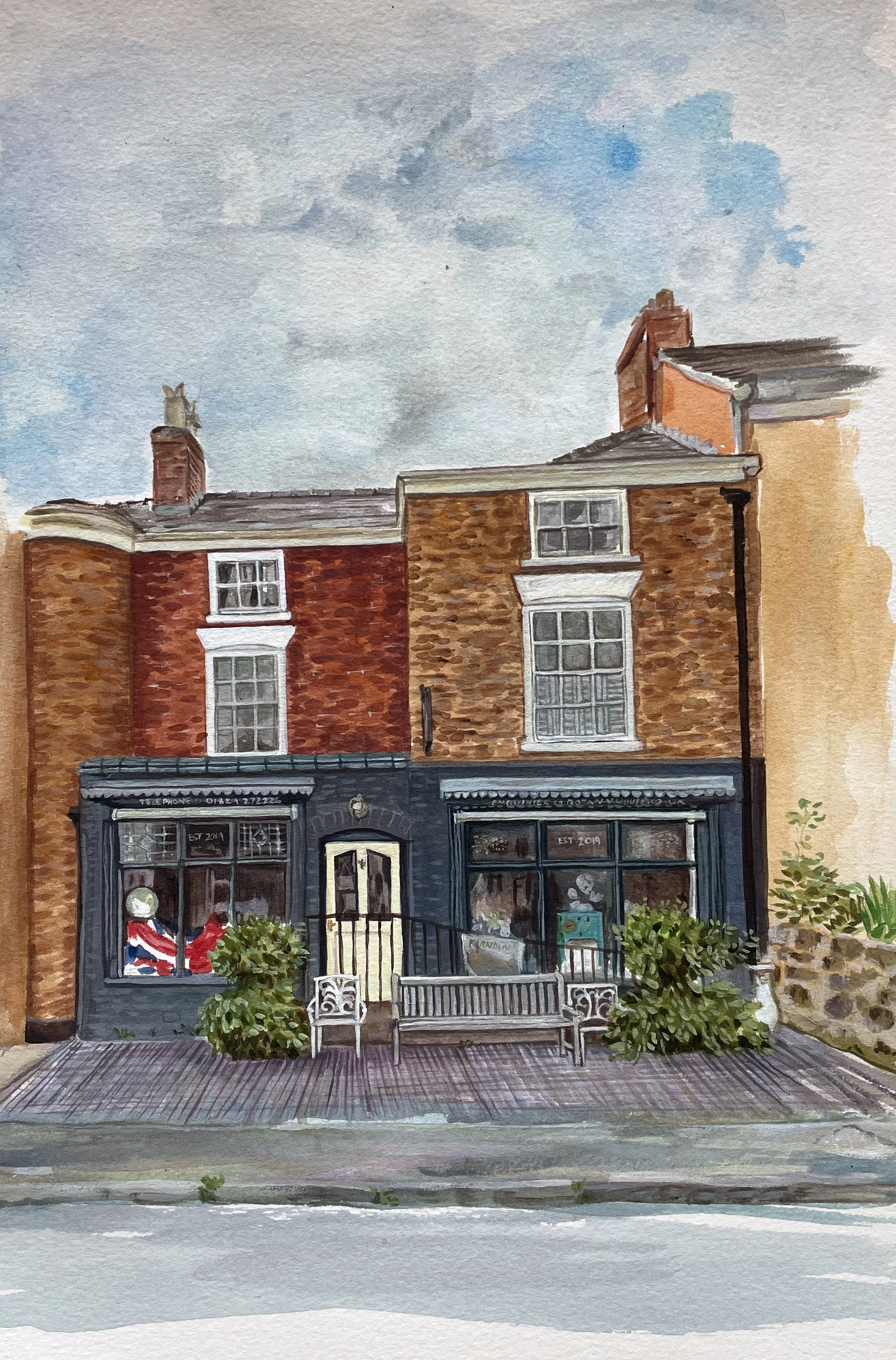 Watercolor painting of a two-story brick building with large front windows, white window frames, a cream-colored door, and outdoor seating with two benches and green plants, under a cloudy sky.