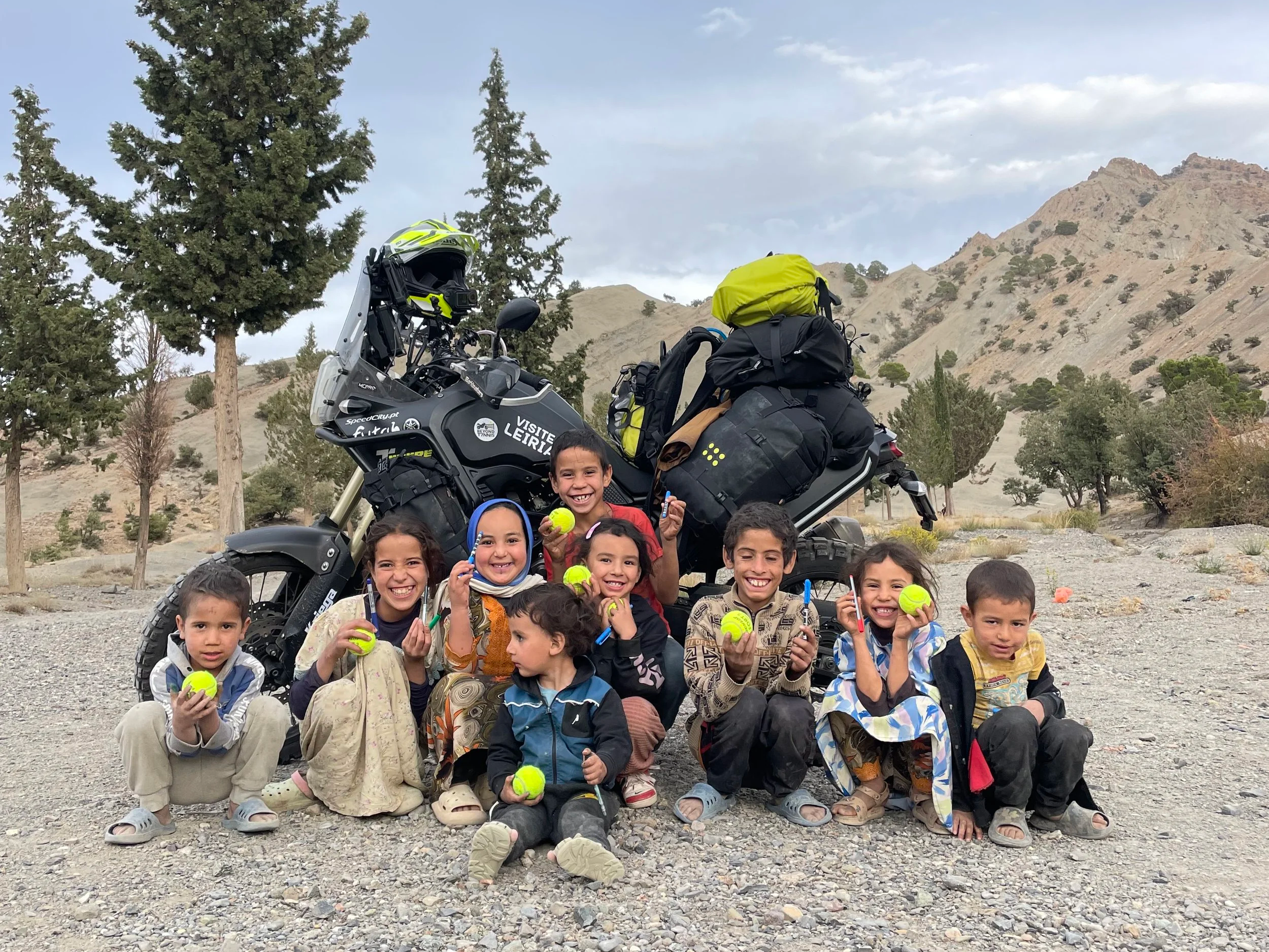 Yamaha Ténére 700 motorcycle with kriega luggage next to a big group of kids holding tennis balls in the High Atlas in Morocco, close to Imilchil
