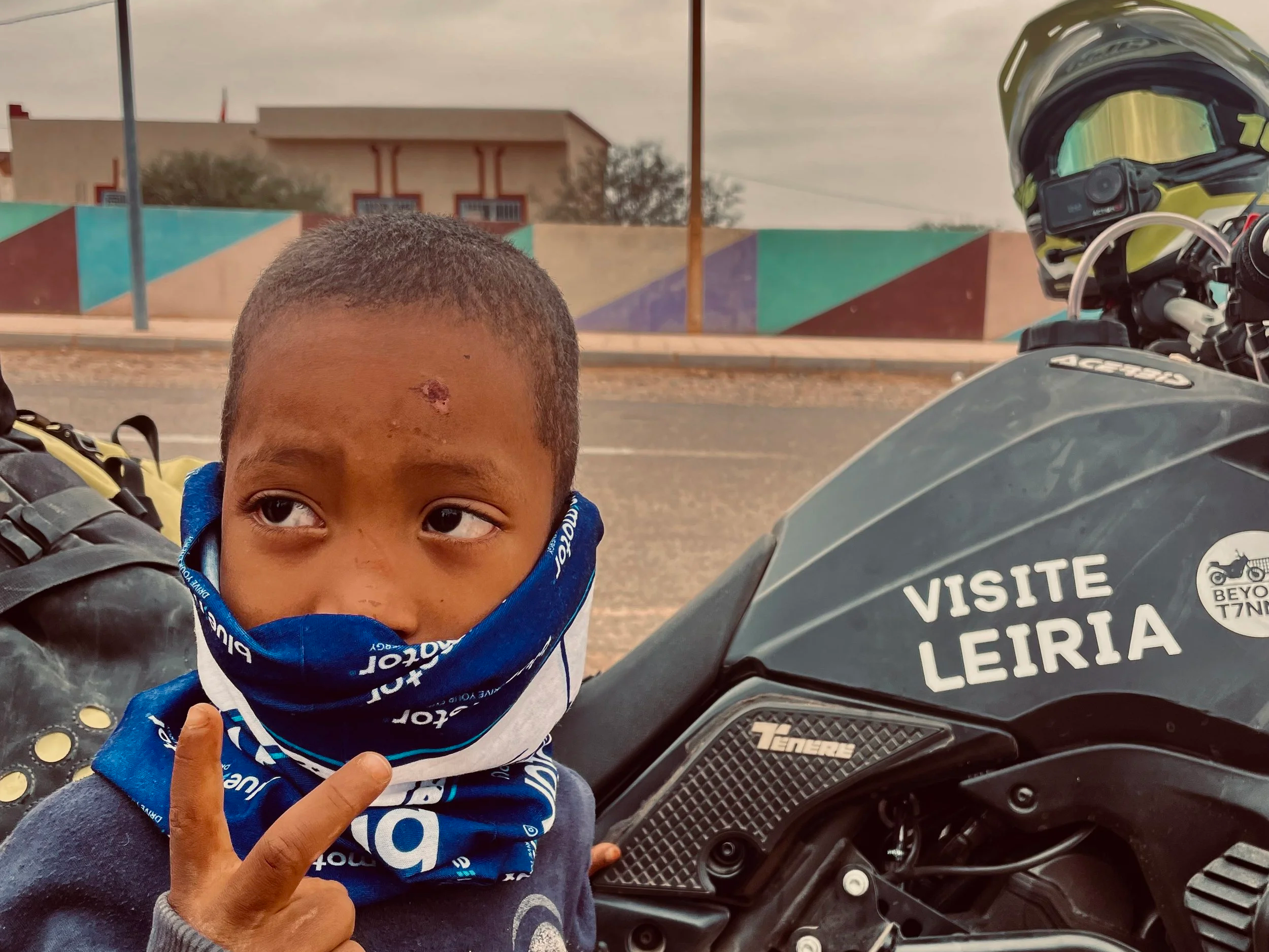 Kid with a neck tube from bluemotor next to a Yamaha Ténére 700 motorcycle during Beyond T7nnis 