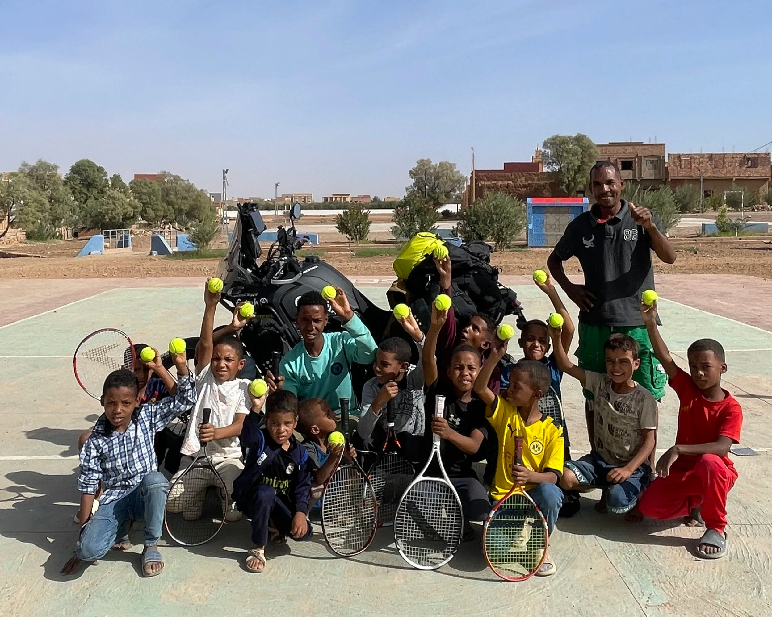 Yamaha Ténére 700 motorcycle with a group of kids  holding donnated tennis rackets and balls, during a Beyond T7nnis Mission in Morocco