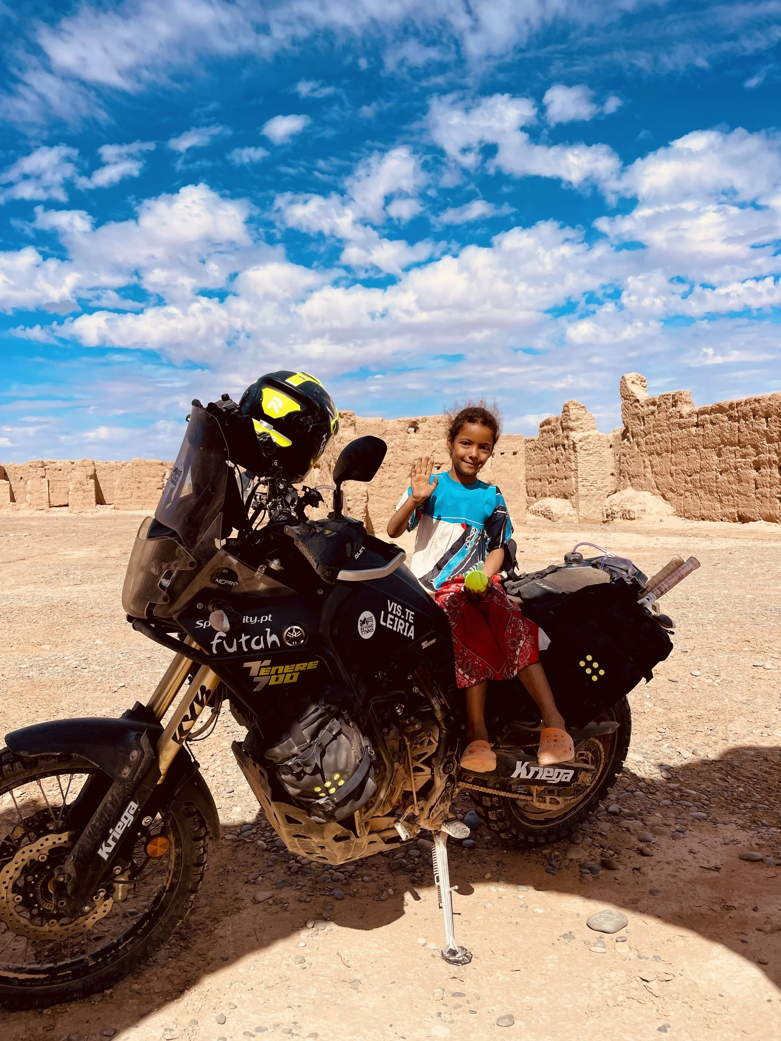 Yamaha Ténére 700 motorcycle with a little girl on it holding a tennis ball, between erfoud and Merzouga in Morocco, during a Beyond T7nnis Mission